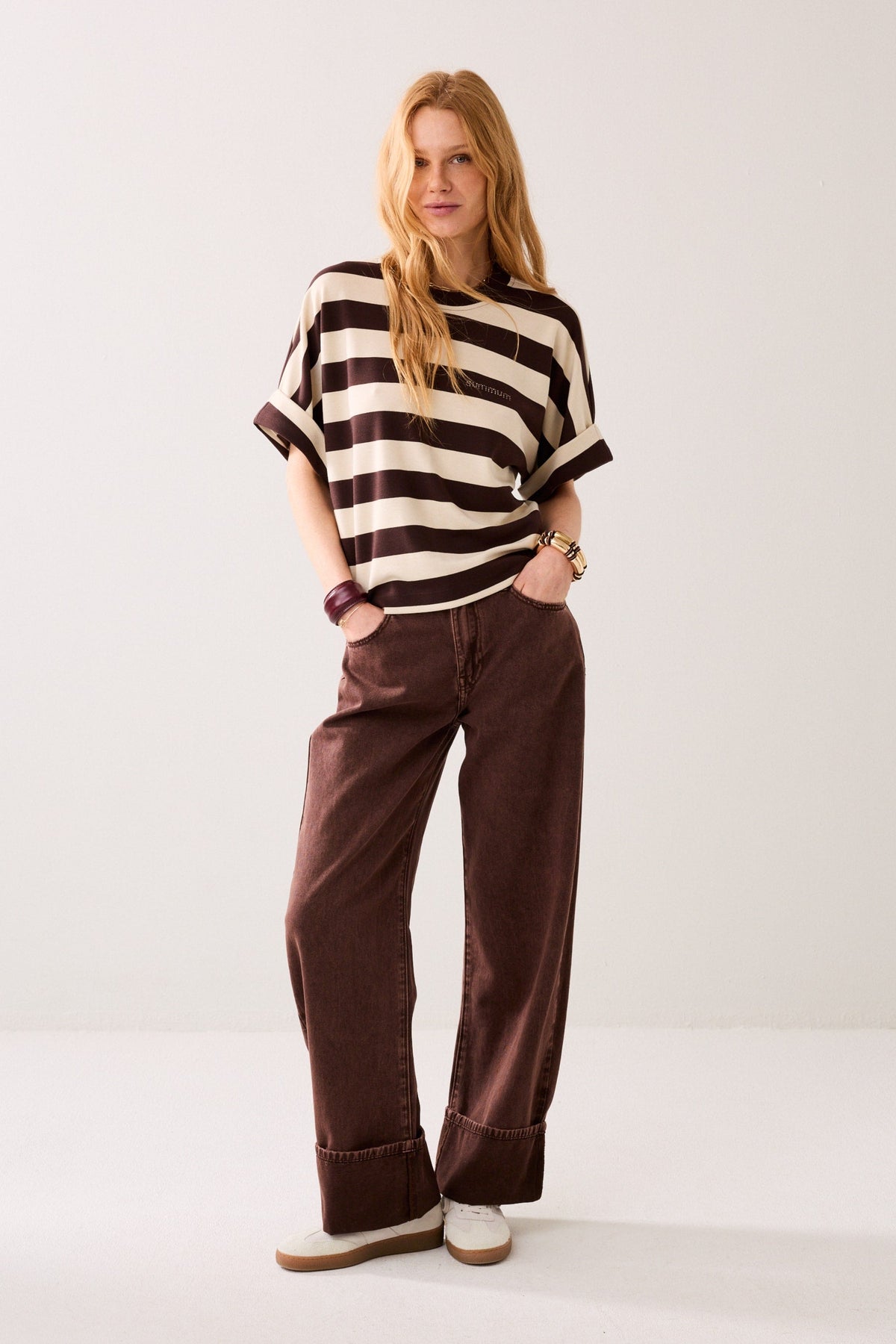 Woman wearing a short-sleeve crewneck t-shirt with horizontal dark brown and cream stripes,  displayed on a plain background.
