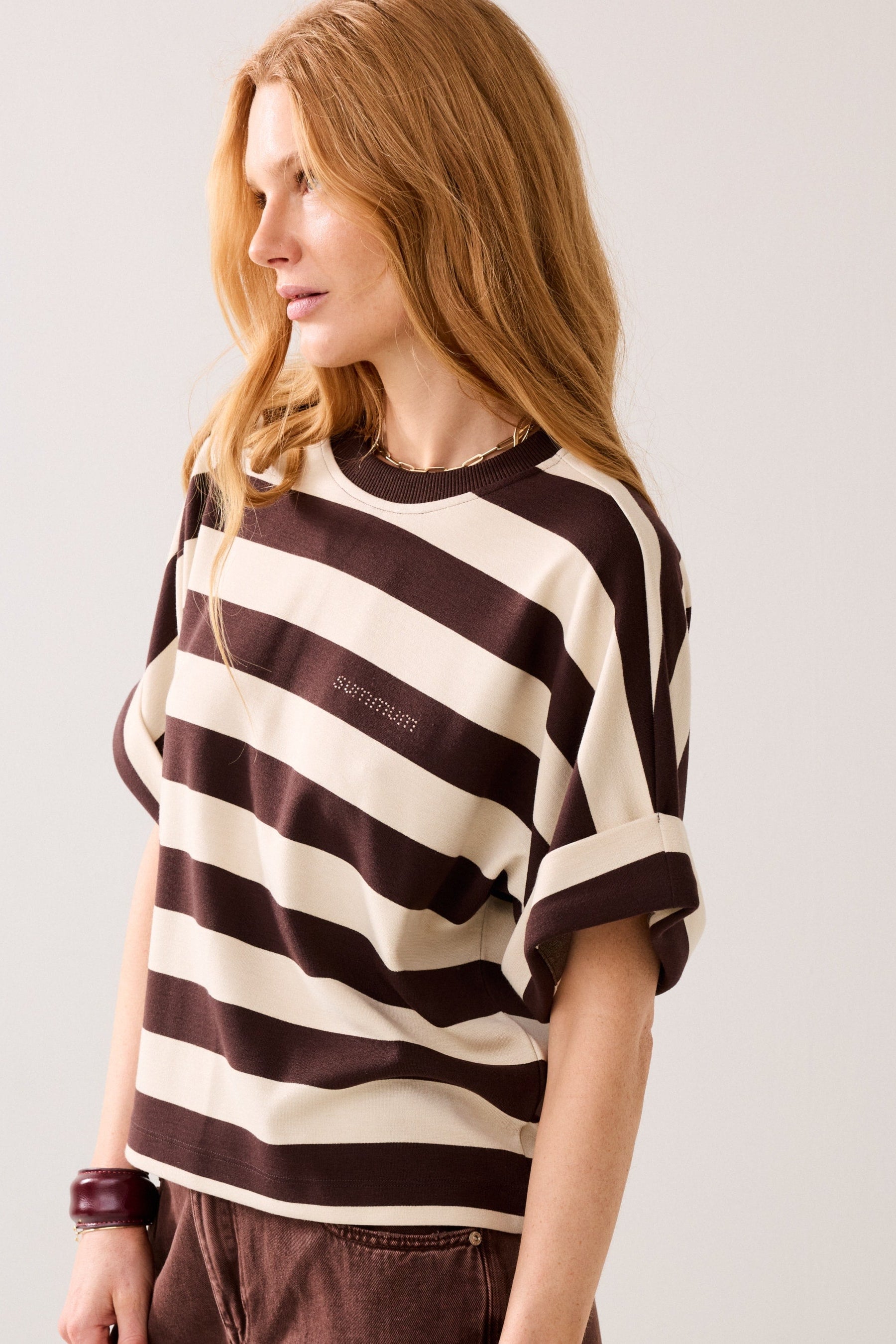 Woman wearing a short-sleeve crewneck t-shirt with horizontal dark brown and cream stripes, featuring a small embroidered 'summum' logo on the left chest, displayed on a plain background.