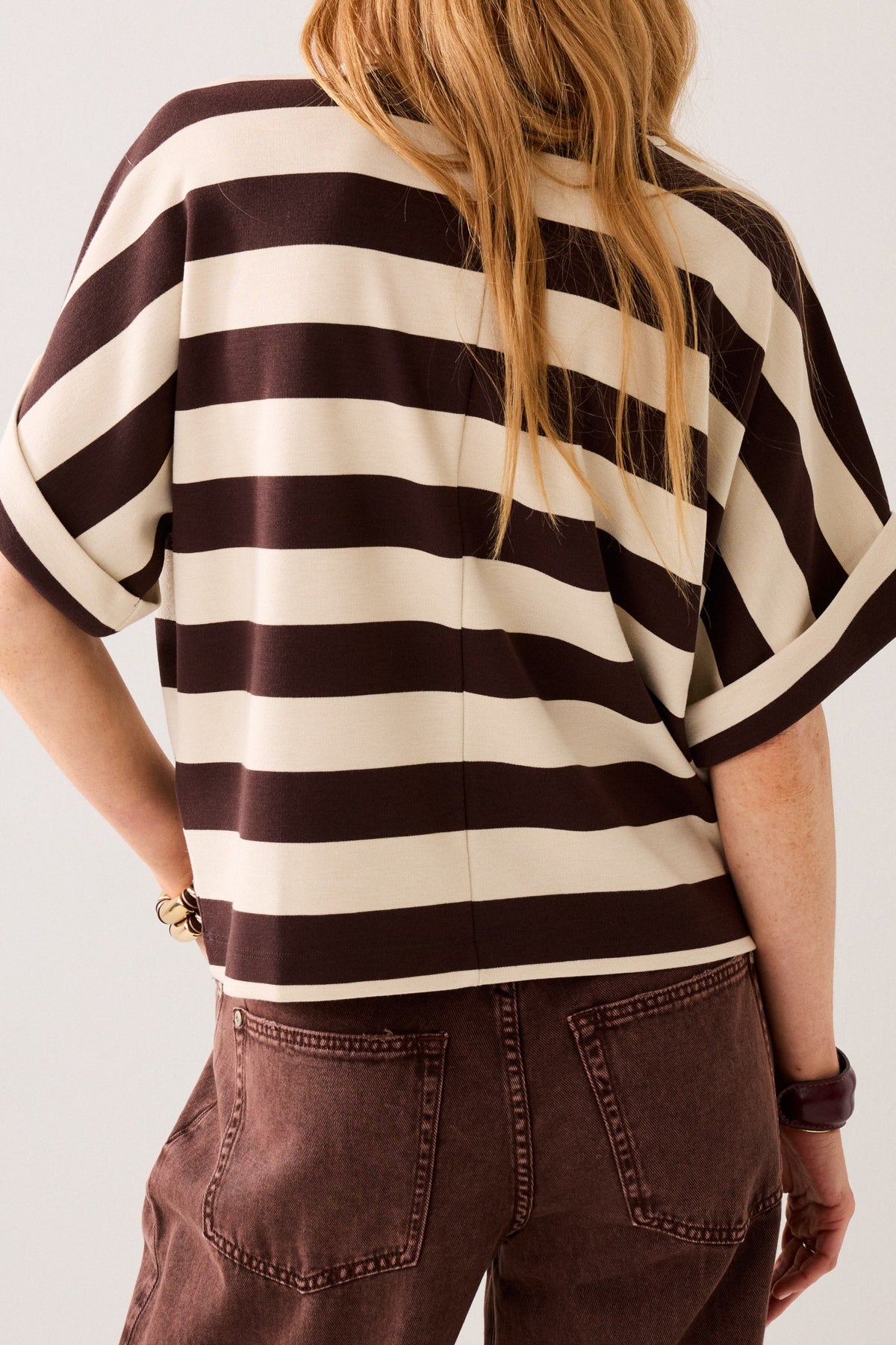 Woman shown from the back wearing a short-sleeve crewneck t-shirt with horizontal dark brown and cream stripes,  displayed on a plain background.