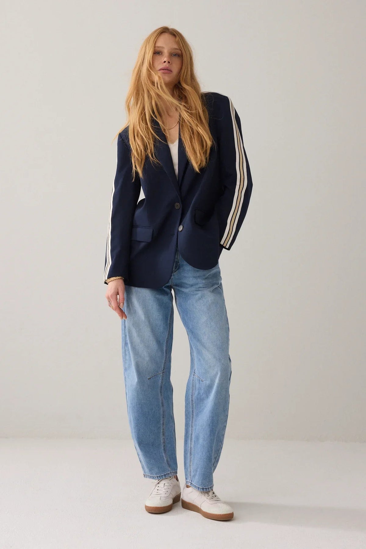 A woman wearing a navy blue blazer with signature three-stripe detailing on the sleeves, featuring beige and white stripes, shown against a plain white background.