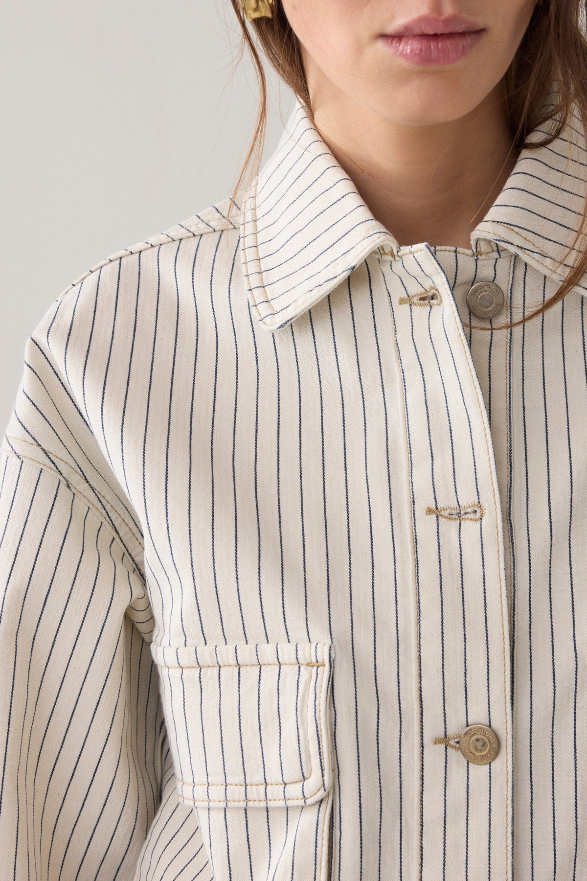 A close up of a women wearing cropped denim jacket wth an ivory base and navy herringbone vertical stripe detail on a plain background.  
