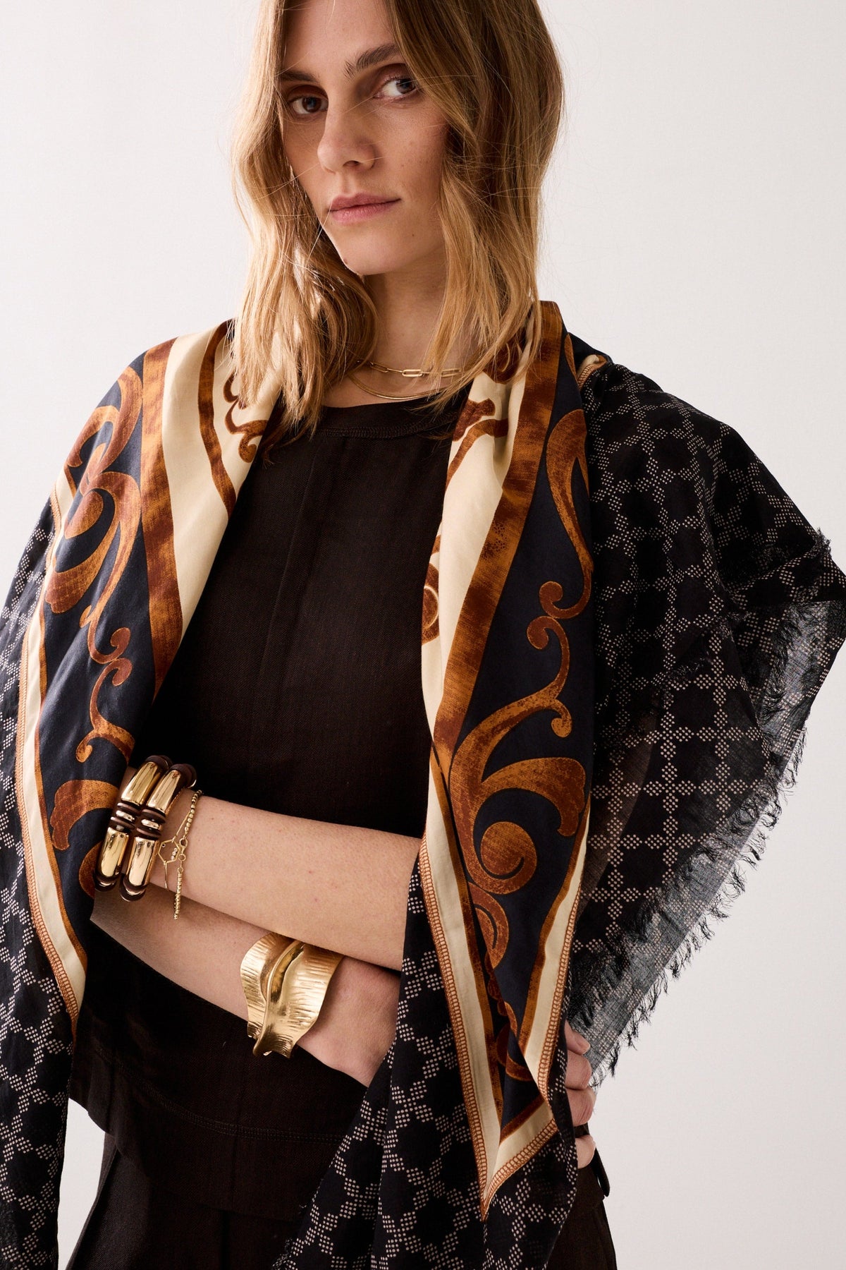 Woman wearing a patterned scarf with gold and black design on a white background