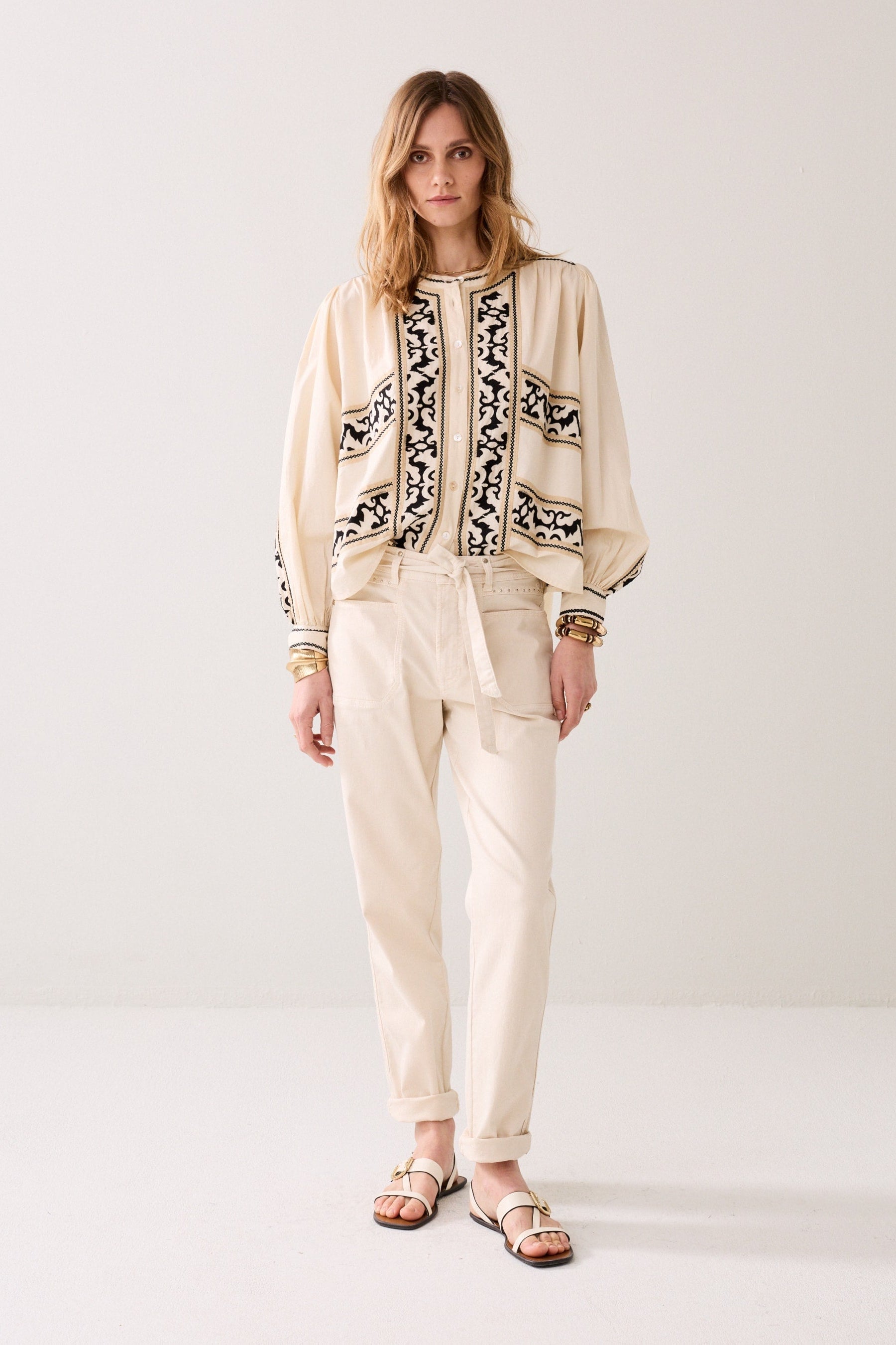 Model wearing a patterned shirt white cropped pants, and sandals on a plain background