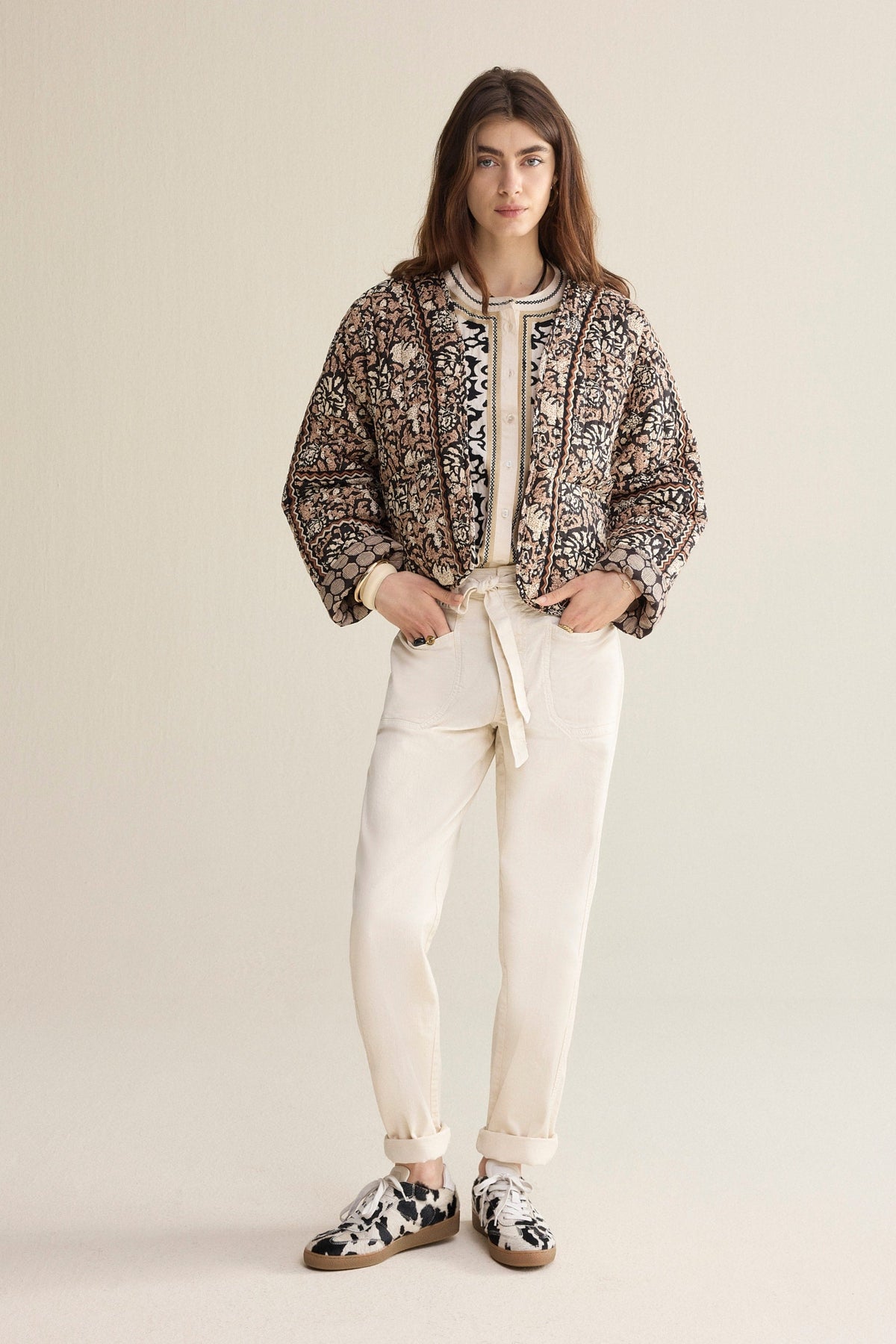 Model wearing a patterned jacket, white cropped pants, and sneakers on a plain background
