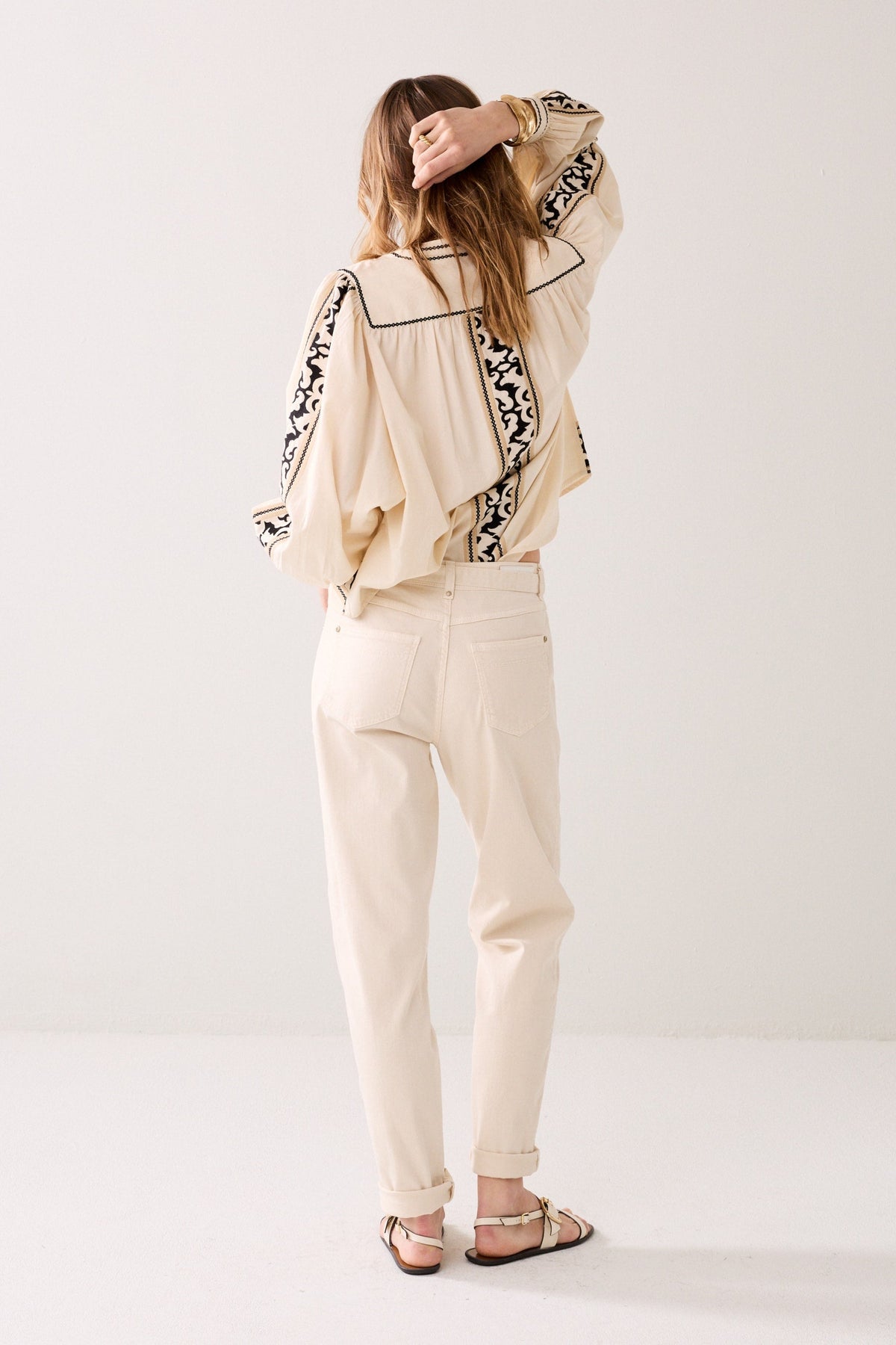Model shown from the back wearing a patterned shirt white cropped pants, and sandals on a plain background