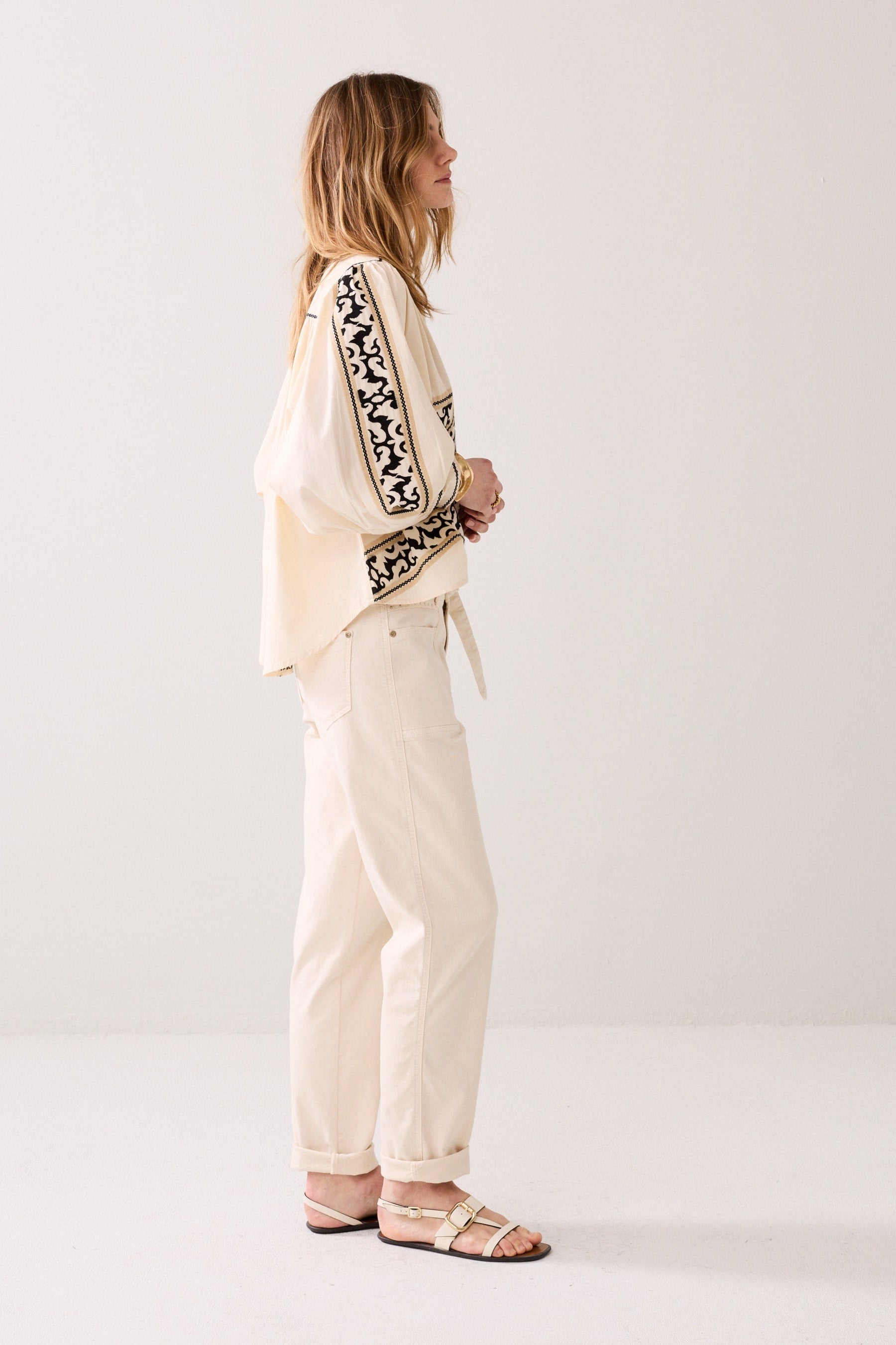Model wearing a patterned shirt shown from the side , white cropped pants, and sandals on a plain background