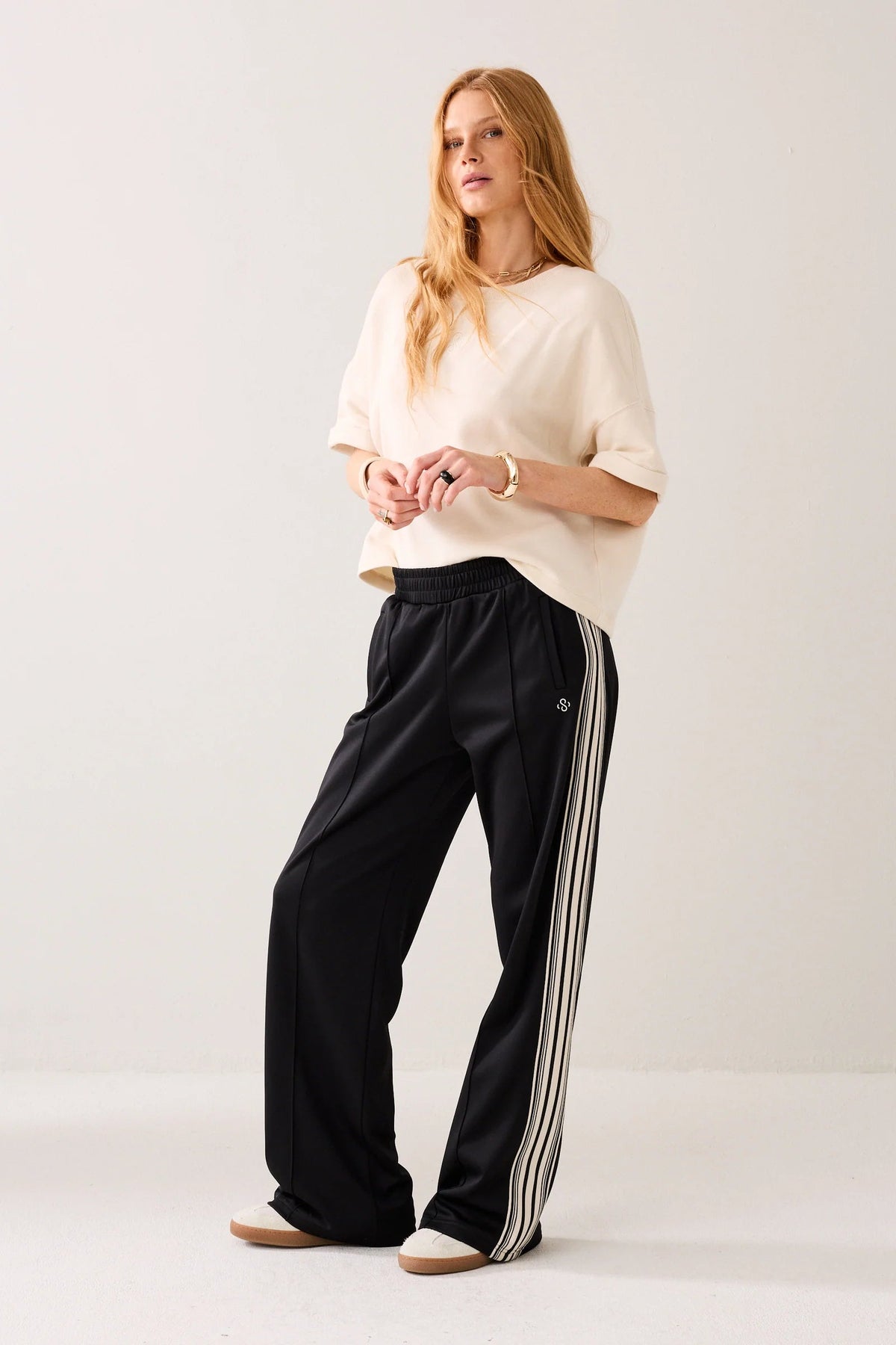 Woman wearing a white top and black pants with stripes on a plain background