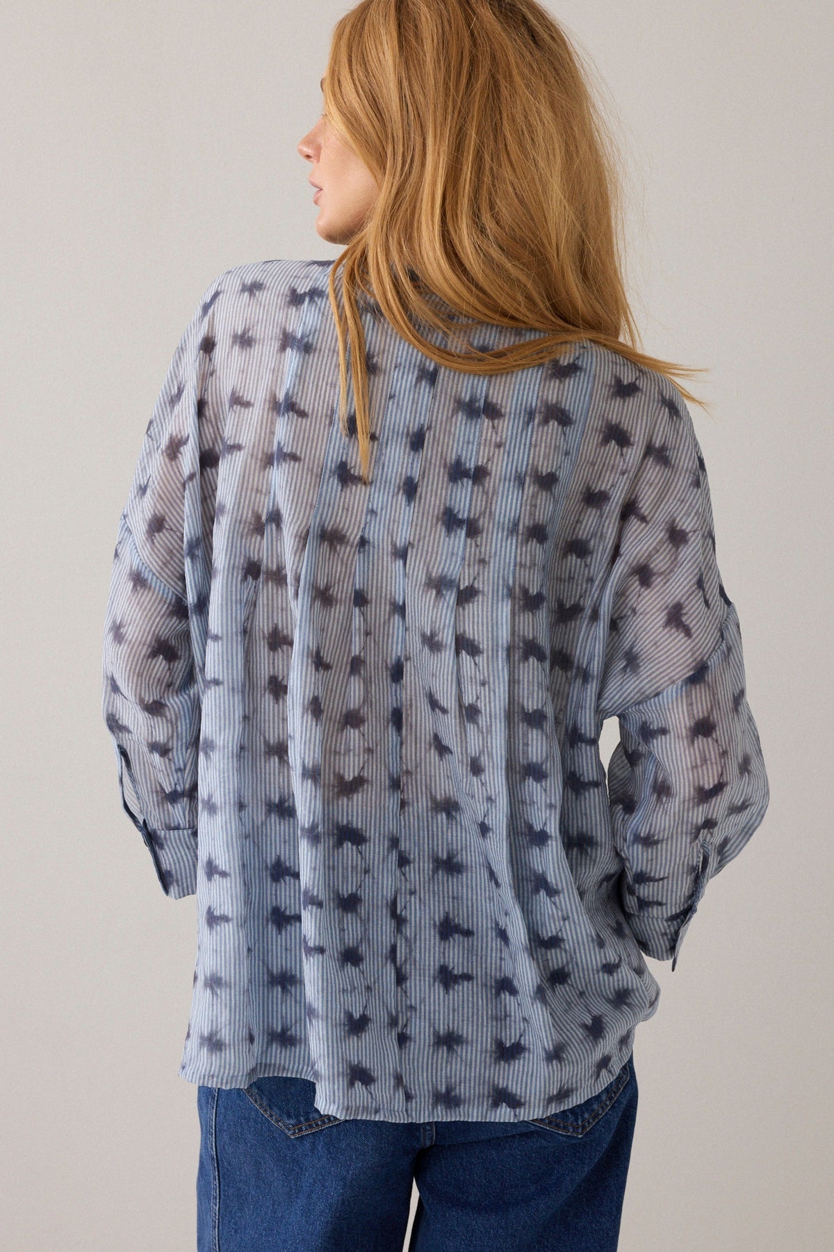 Women shown from the back wearing a light blue stripe pattern blouse with 3/4 sleeves and dark blue denim jeans on a plain background.