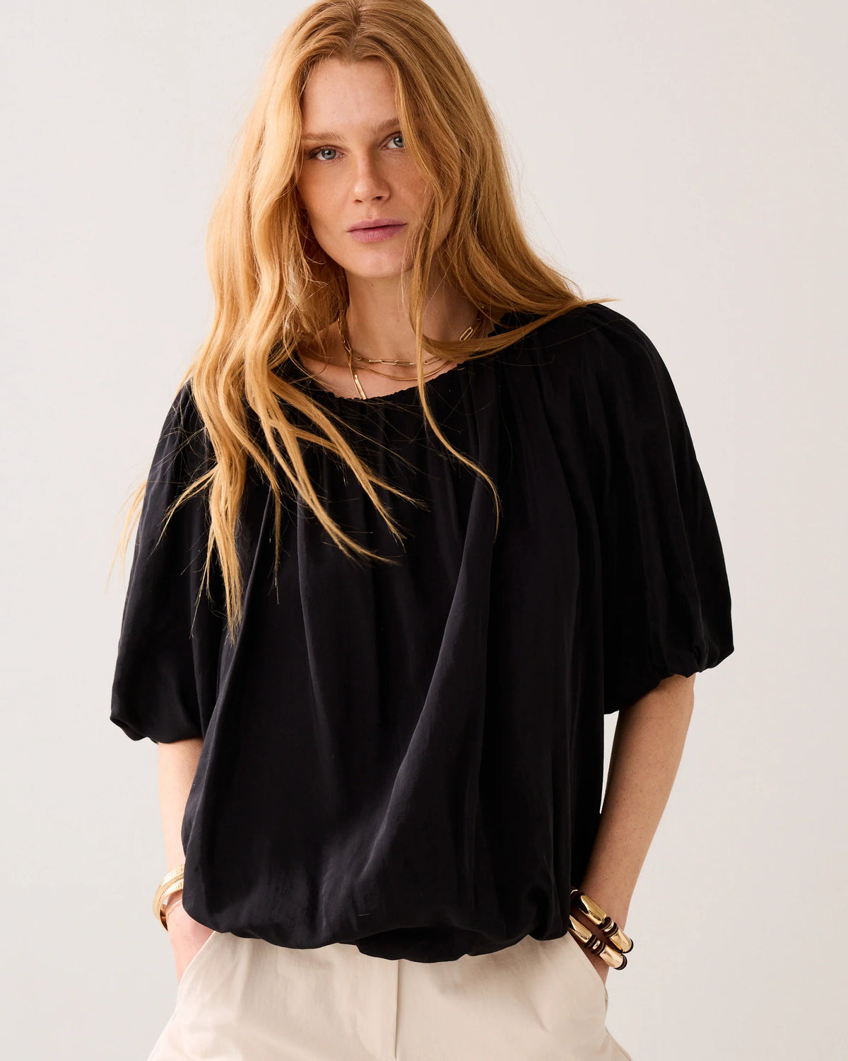 Model wearing a black blouse with puff sleeves  and cream tailored pants on a light background
