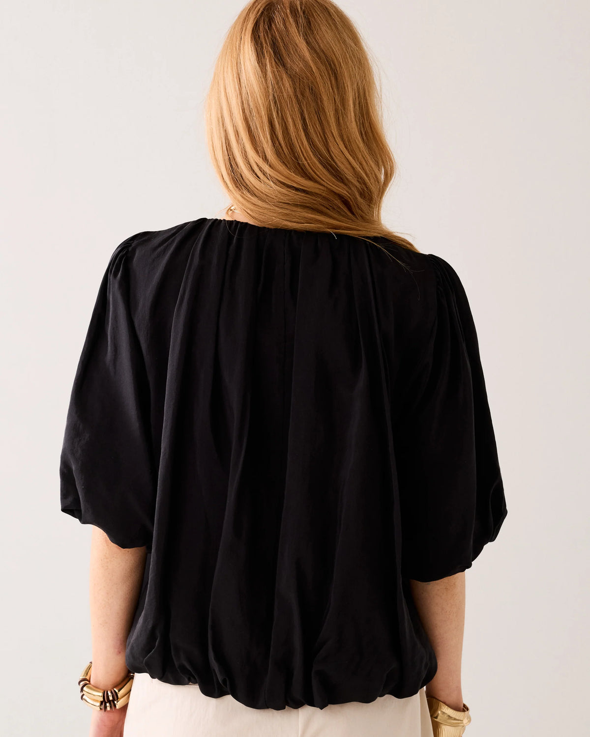 Model  shown from the back wearing a black blouse with puff sleeves  and cream tailored pants on a light background