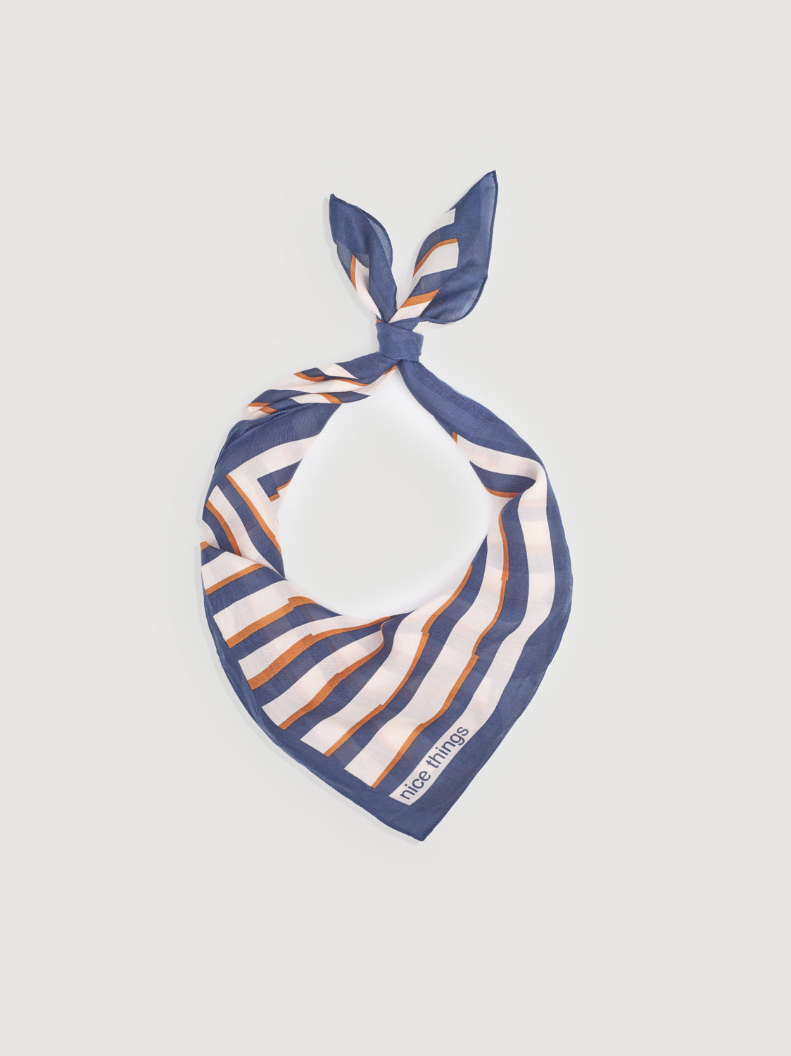 A square scarf tied with a geometric pattern of navy blue, white, and orange stripes, laid flat against a light grey background. The brand name 'nice things' is visible in the bottom-left corner.