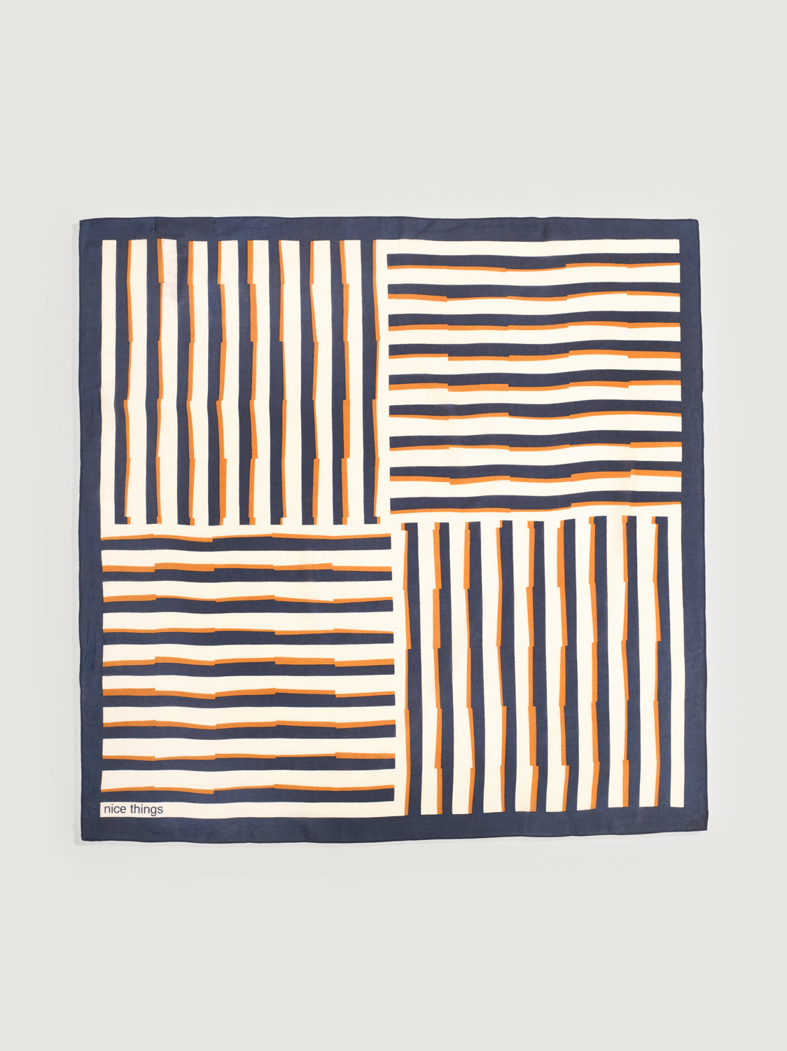 A square scarf with a geometric pattern of navy blue, white, and orange stripes, laid flat against a light grey background. The brand name 'nice things' is visible in the bottom-left corner.