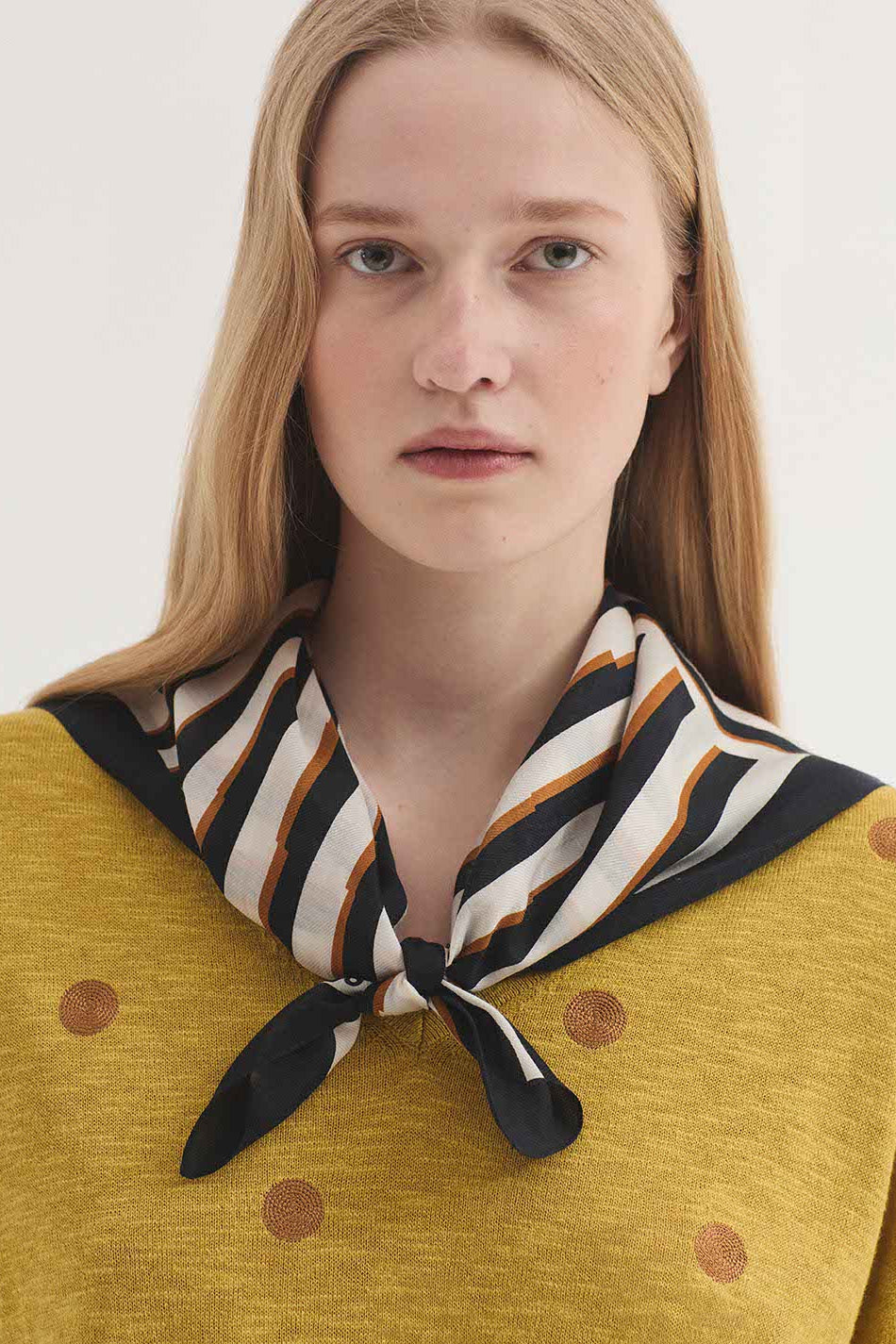 Model wearing a scarf around her shoulders in cream, navy and tan stripe up close on a plain background. 