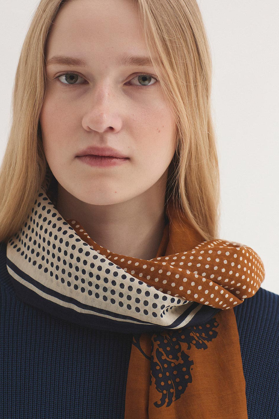 Woman wearing a patterned scarf on a plain background