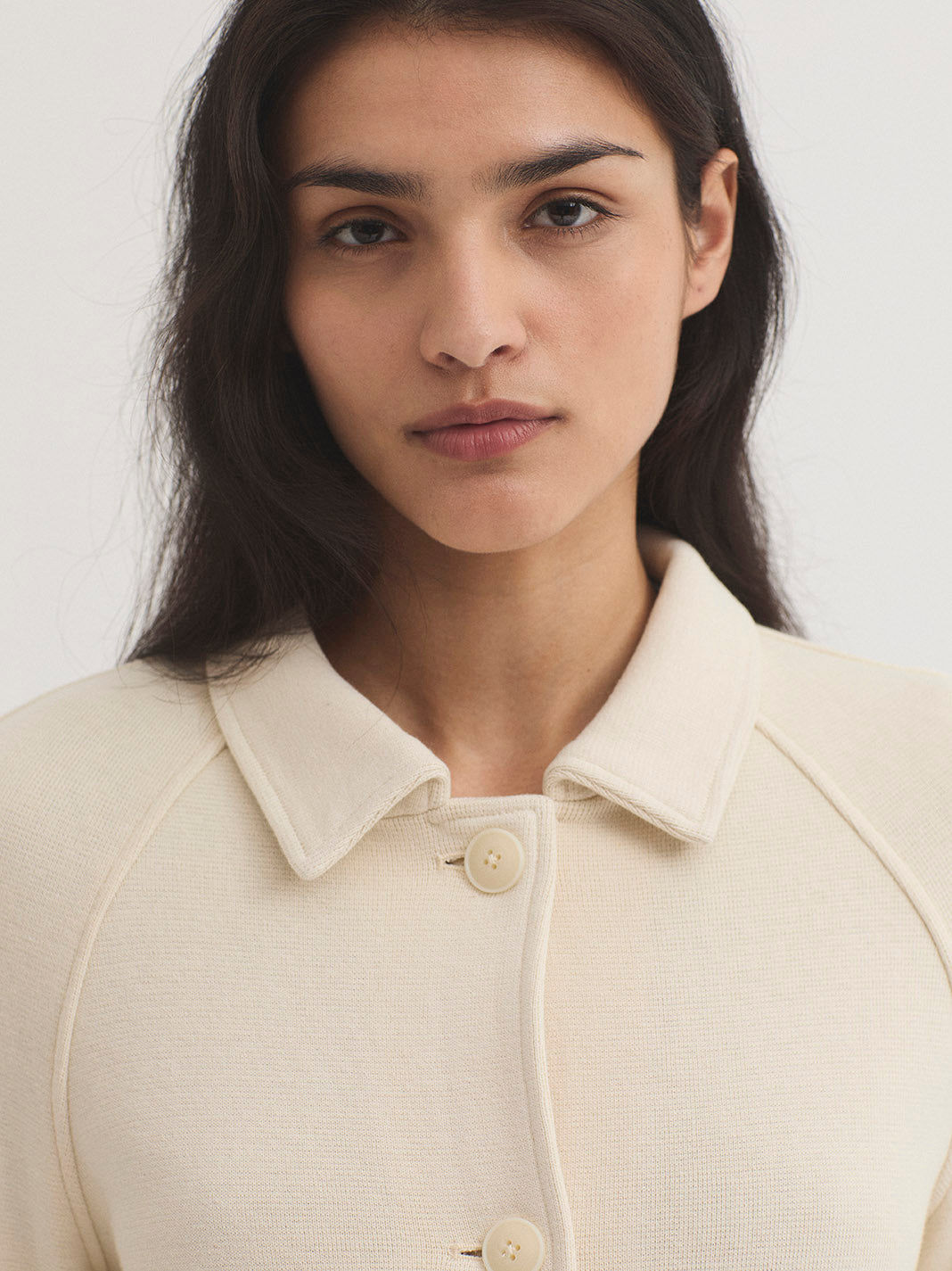 Woman wearing a beige knit jacket with a plain background