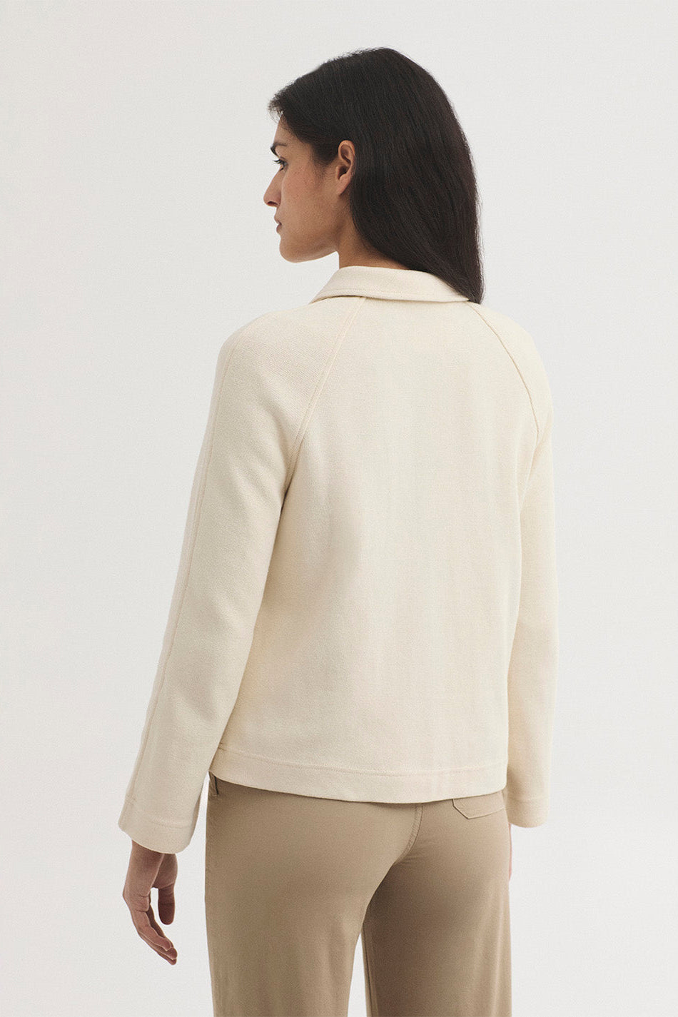 Woman shown from the back wearing a beige knit jacket and tan pants on a white background