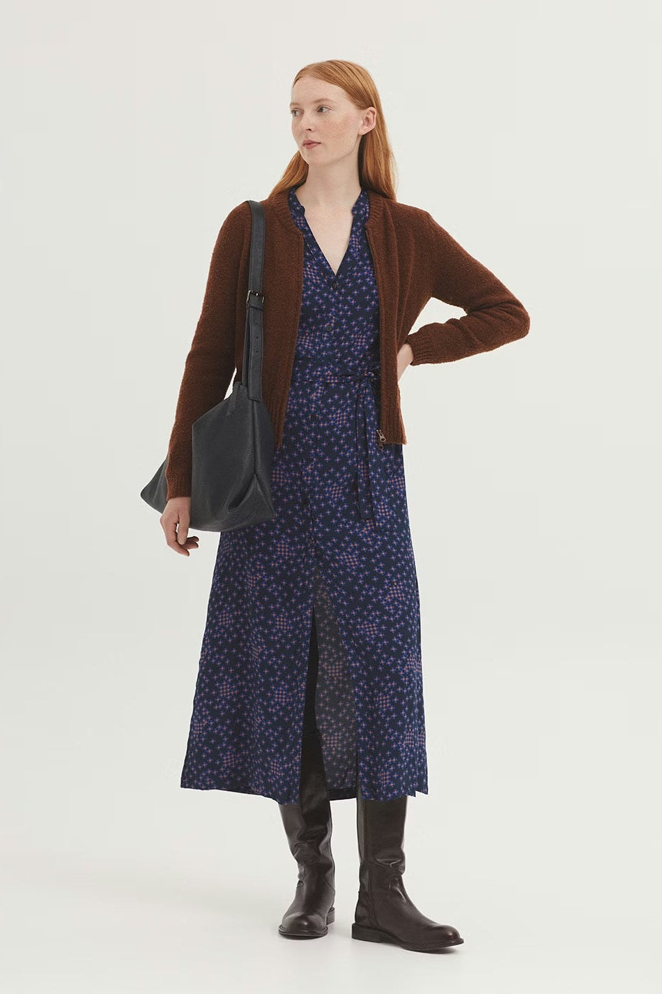 Woman wearing a brown cardigan, blue dress, and black boots on a white background
