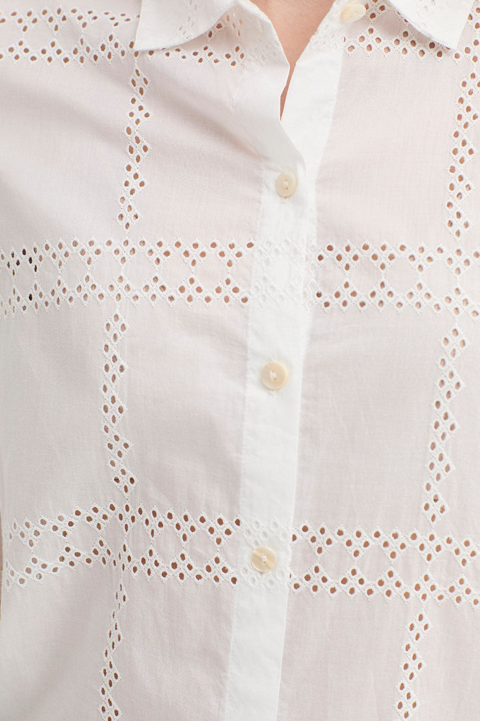 Close-up of a white eyelet button-up shirt with a pointed collar and decorative cutwork pattern.