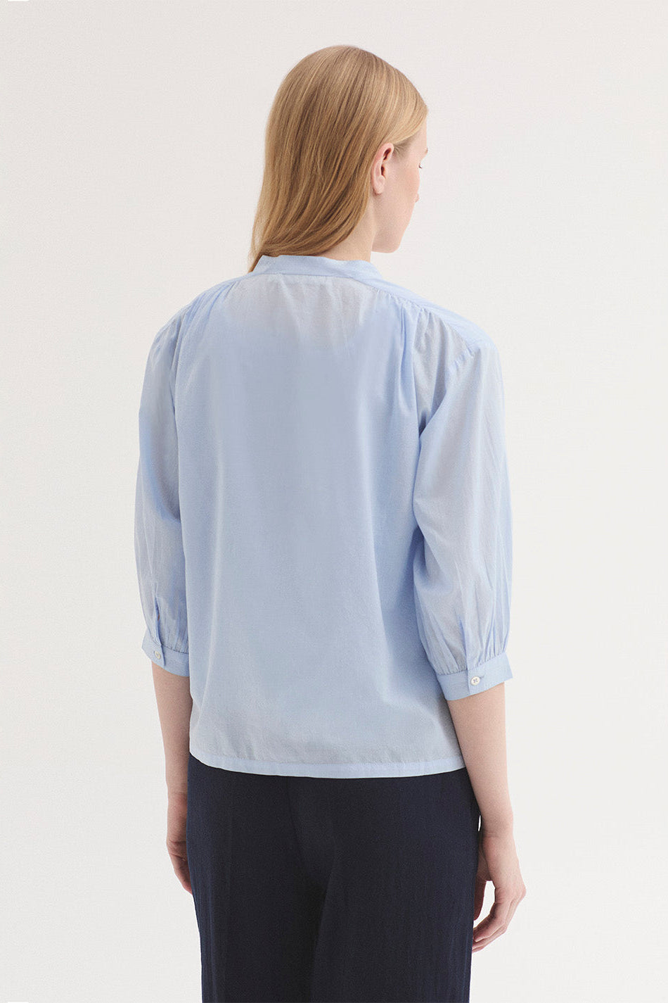 Person wearing a light blue blouse with long sleeves on a plain background