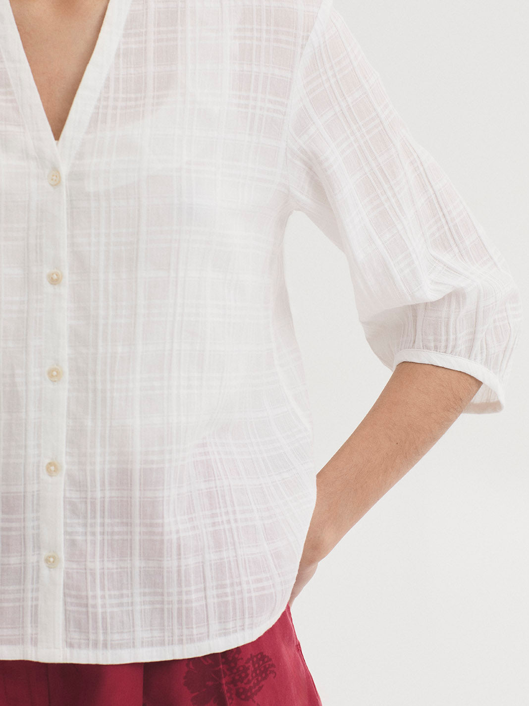 A woman shown from the back wearing a white textured short-sleeve blouse and red floral printed shorts against a plain white studio background.