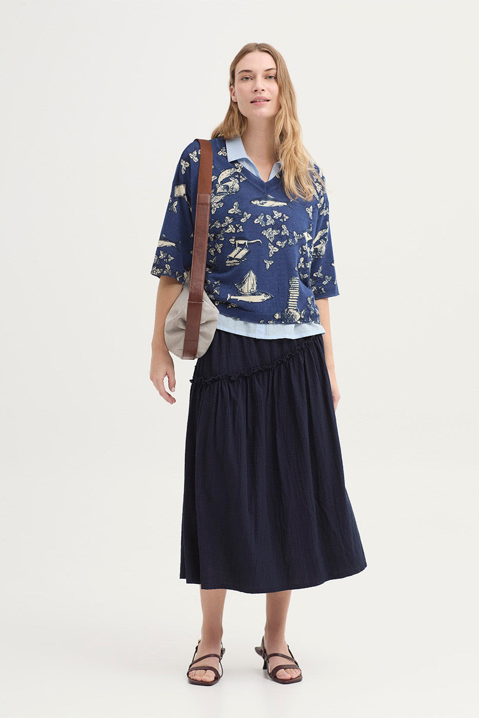 A woman wearing a light blue short-sleeve blouse and a dark navy tiered midi skirt against a plain light background.