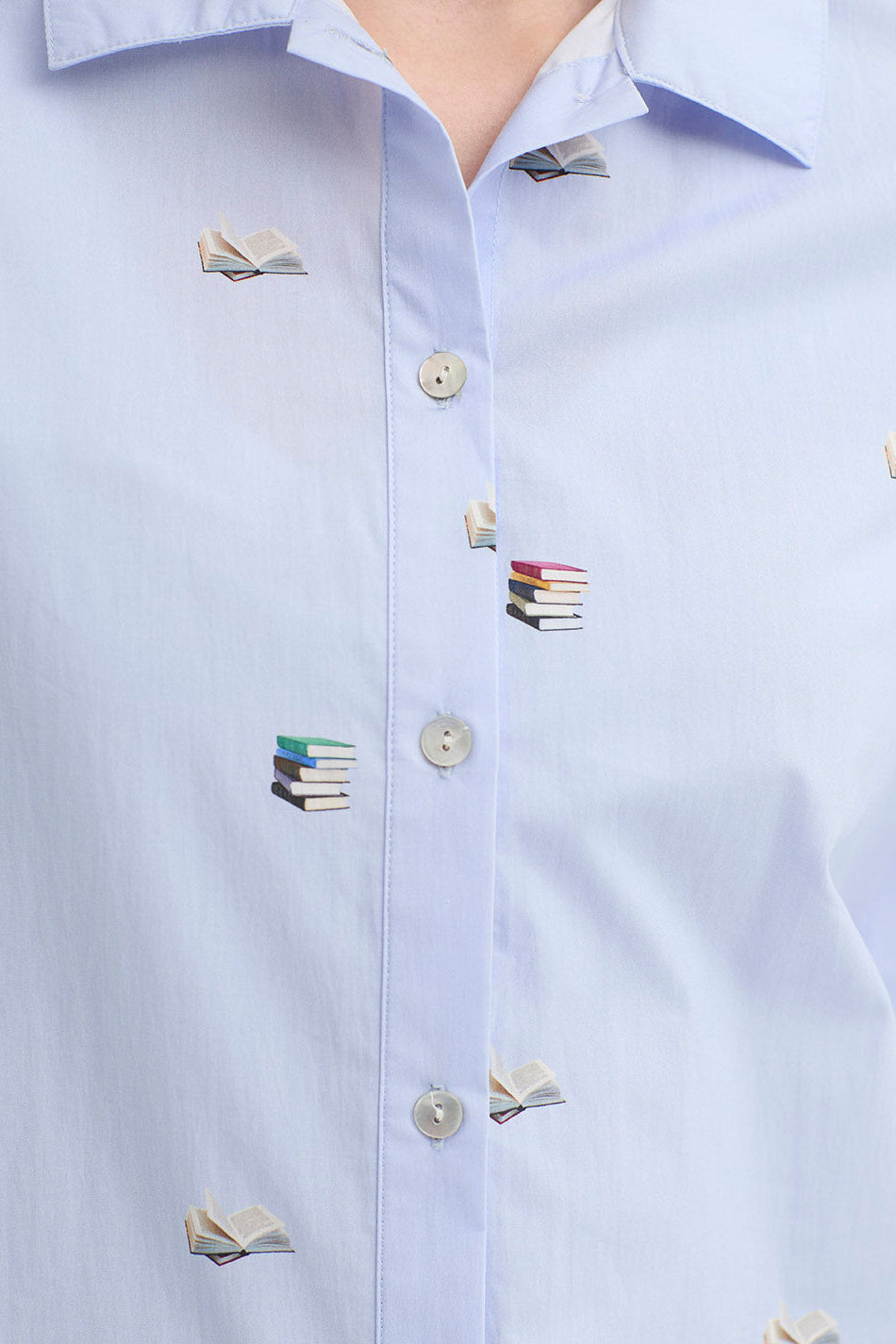 A light blue 3/4 sleeve shirt with delicate books print and mother of pearl buttons on a white background