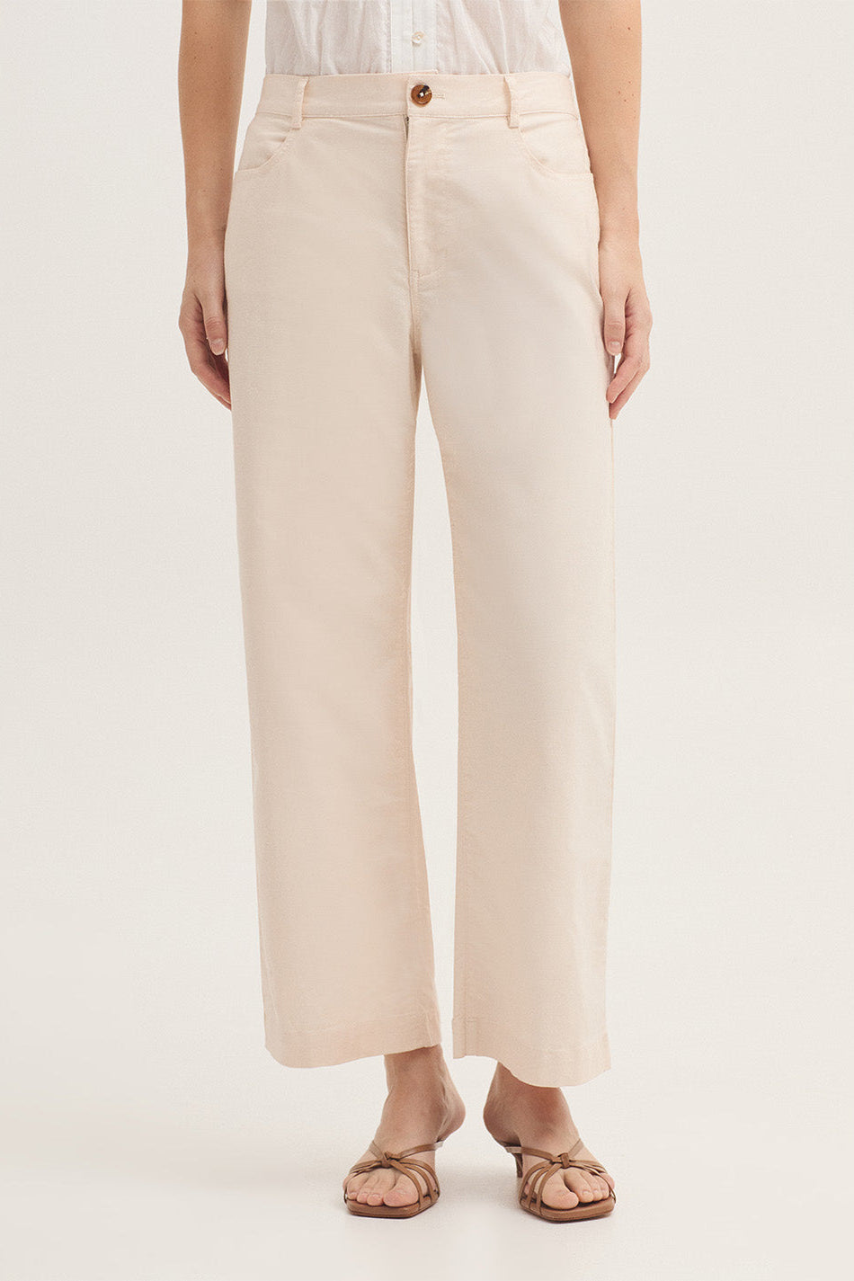 A model wearing a pair of light beige wide-leg cropped pants with a white top and brown sandals, shown from the waist down against a plain white studio background.