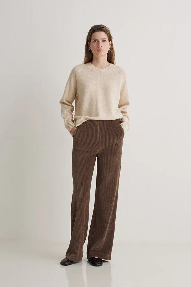 Woman wearing a beige sweater and brown pants on a white background