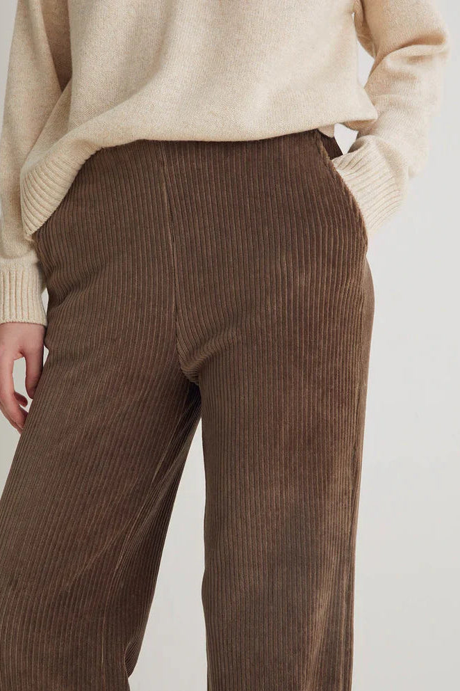 Brown corduroy pants worn with a beige sweater on a plain background