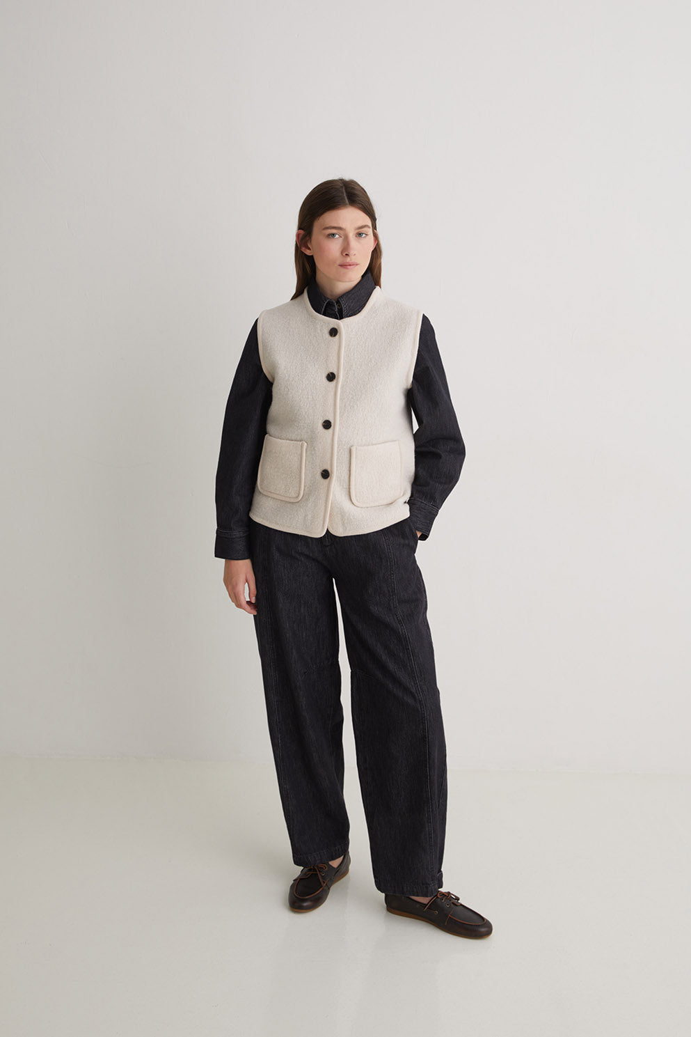Person wearing a white vest over a black shirt and pants on a light gray background