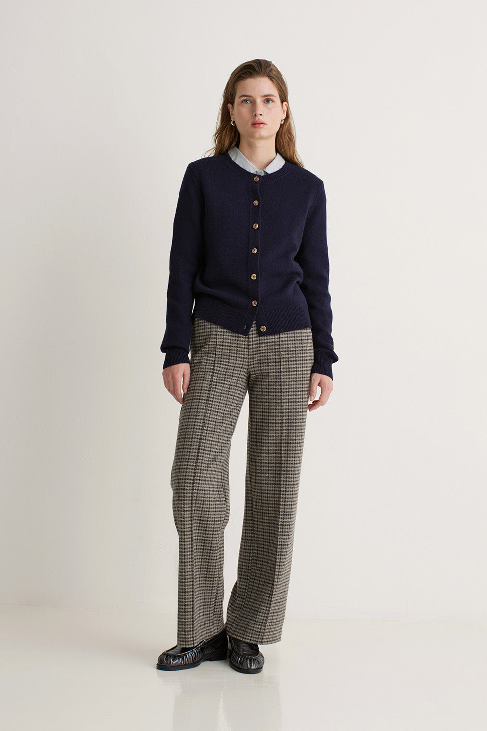 Woman wearing a navy cardigan and plaid pants on a white background