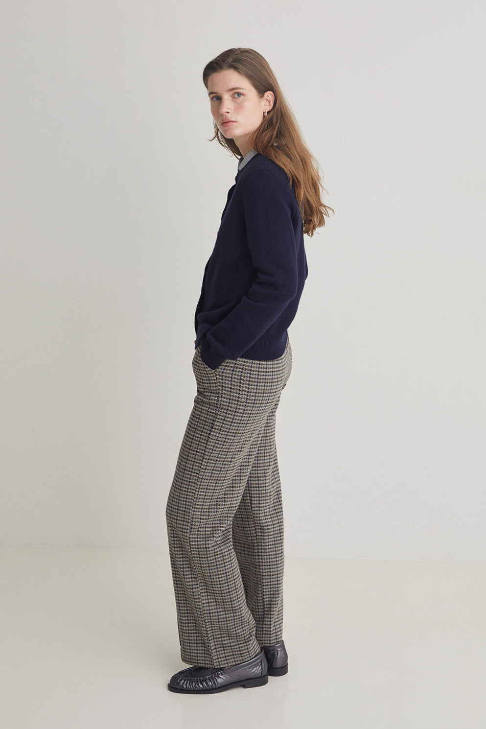 Woman wearing a navy sweater and plaid pants on a light background