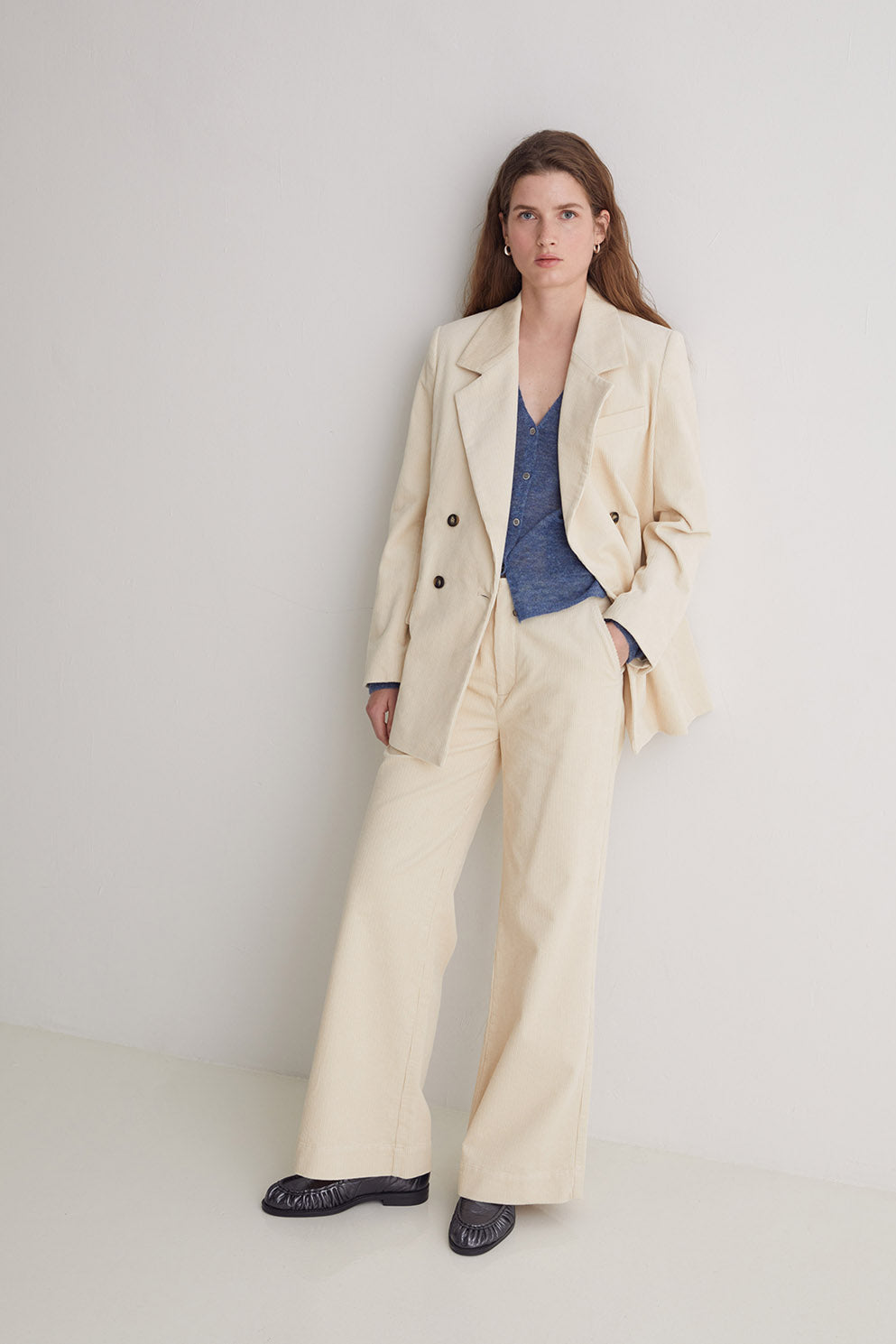 Woman wearing a beige suit with a blue top against a white background