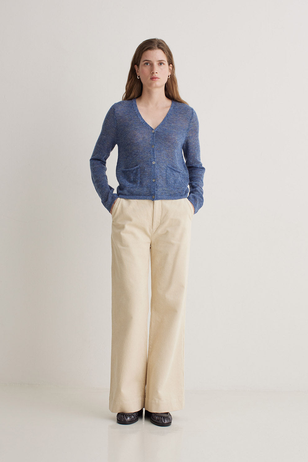 Woman wearing a blue cardigan and beige pants on a white background