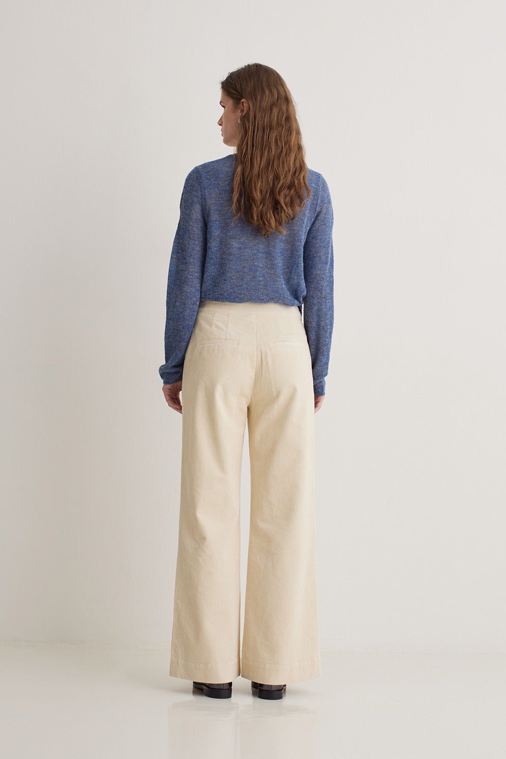 Woman wearing a blue sweater and beige pants on a white background