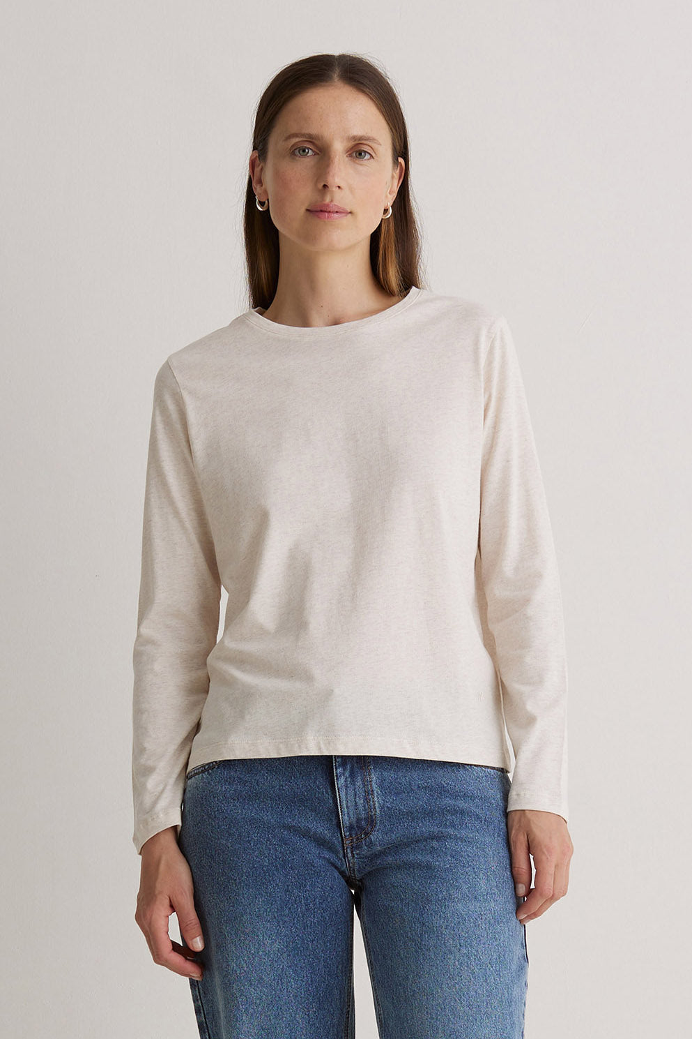 Woman wearing a beige sweater and blue jeans against a plain background