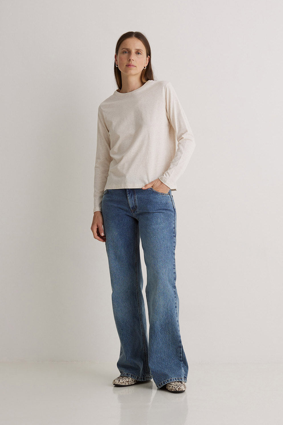 Woman wearing a beige sweater and blue jeans on a white background