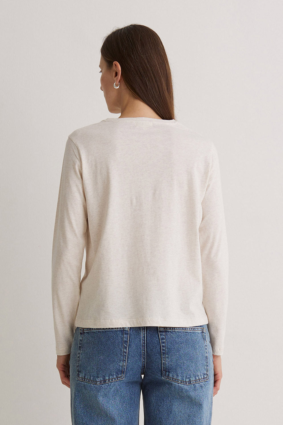 Person wearing a beige sweater and blue jeans on a plain background