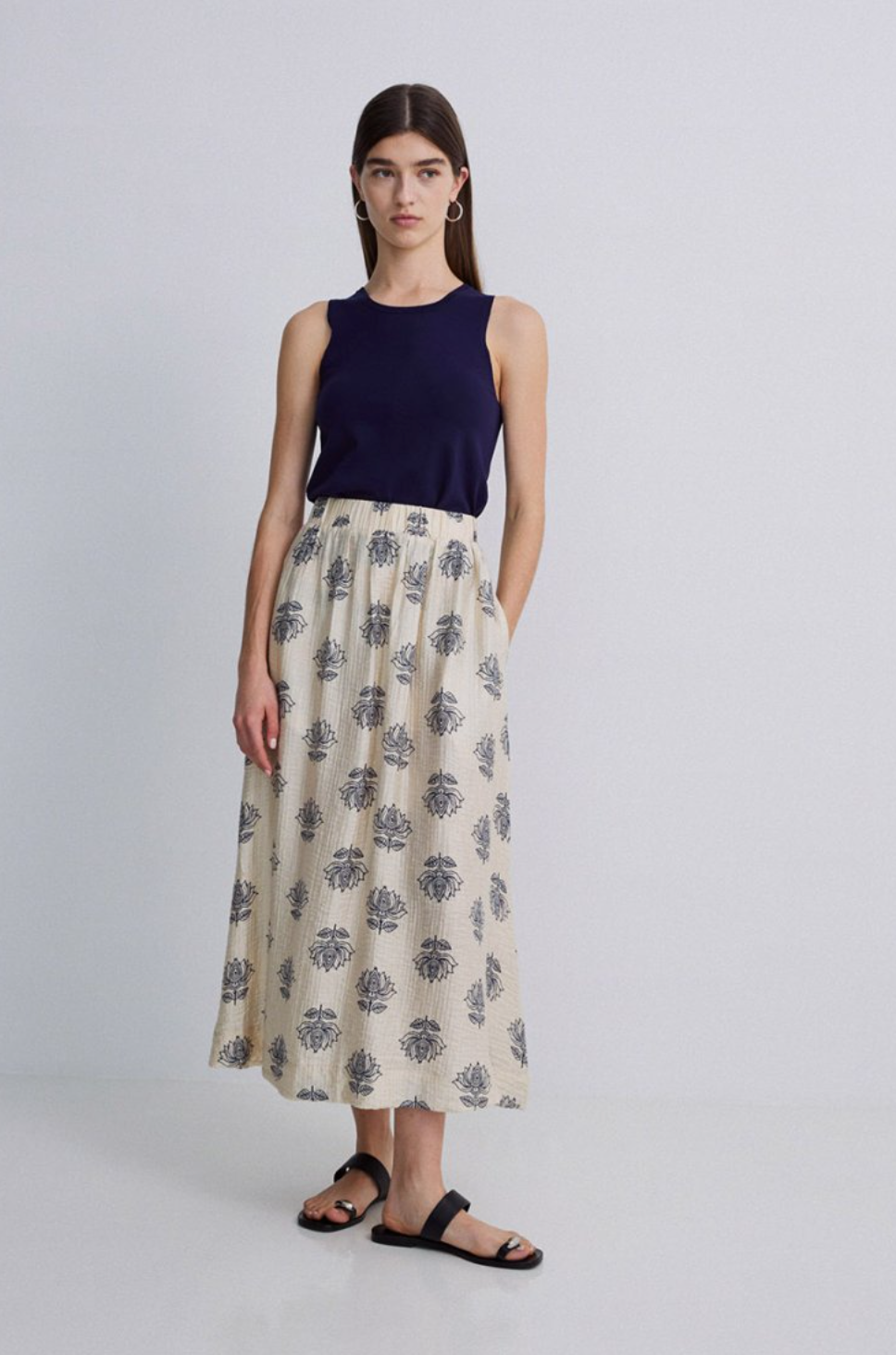Model wearing plain navy tank top with a cream maxi skirt with  a navy floral print on a grey background. 