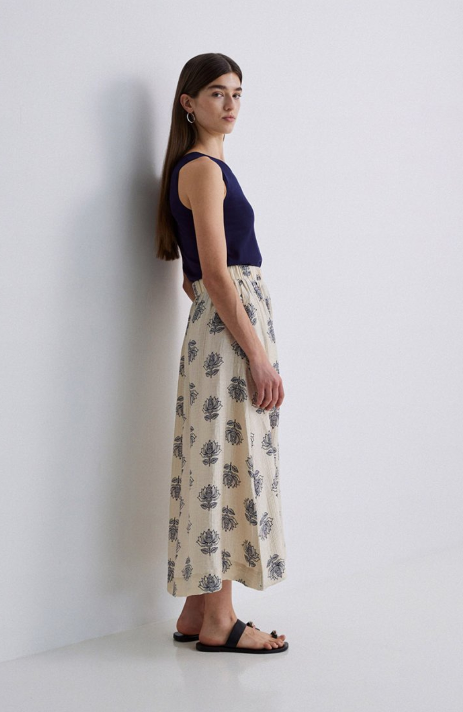 Model wearing plain navy tank top with a cream maxi skirt with  a navy floral print on a grey background. 