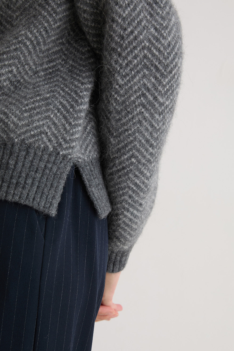 Person wearing a grey turtle neck herringbone sweater and black pants on a white background
