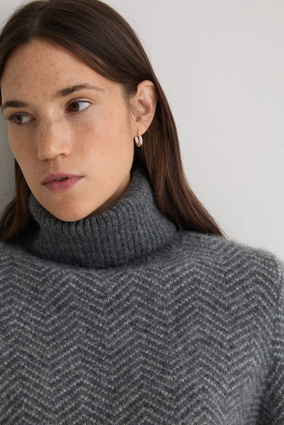 Person wearing a grey turtle neck herringbone sweater and black pants on a white background