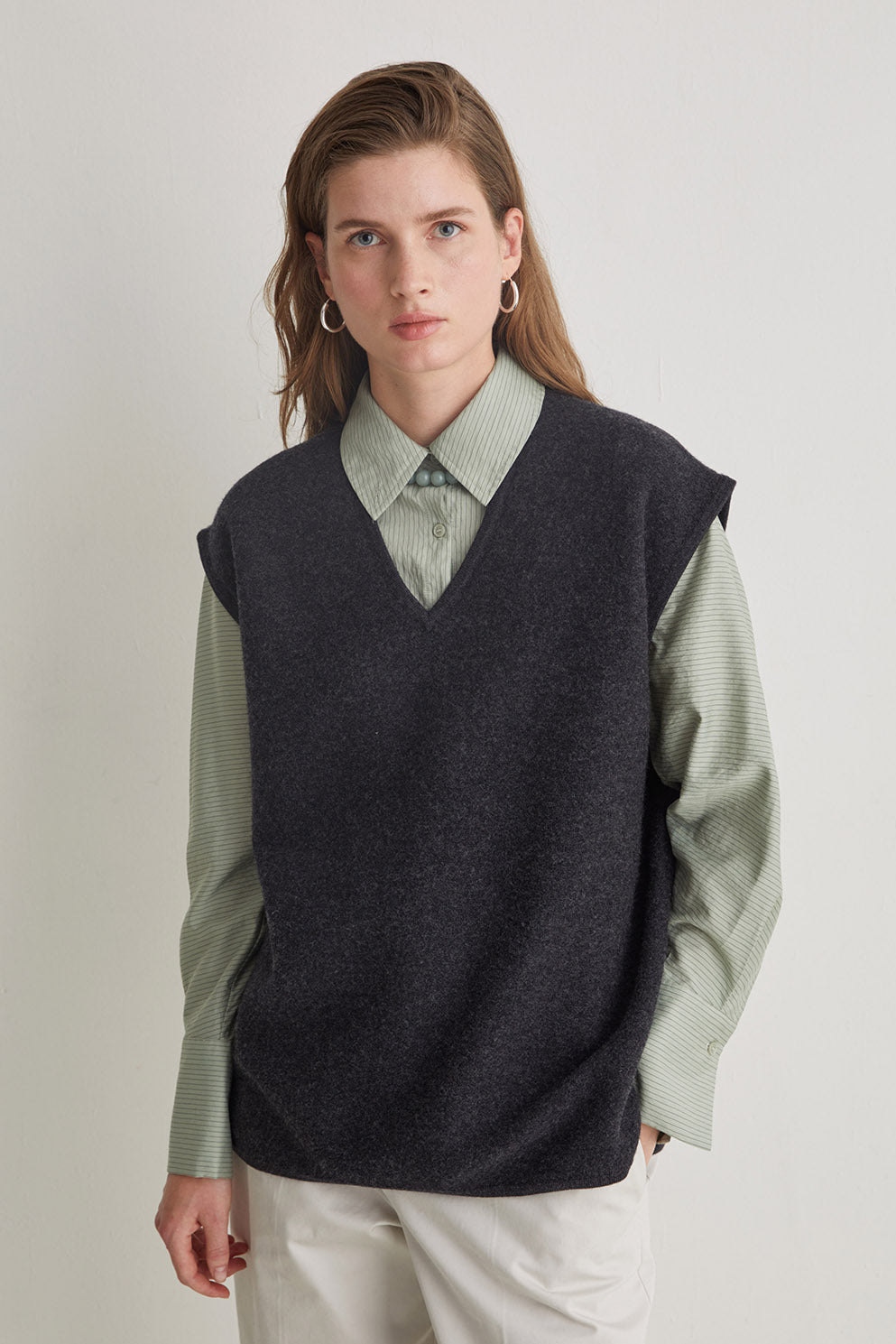 Person wearing a dark gray vest over a light green shirt on a plain background