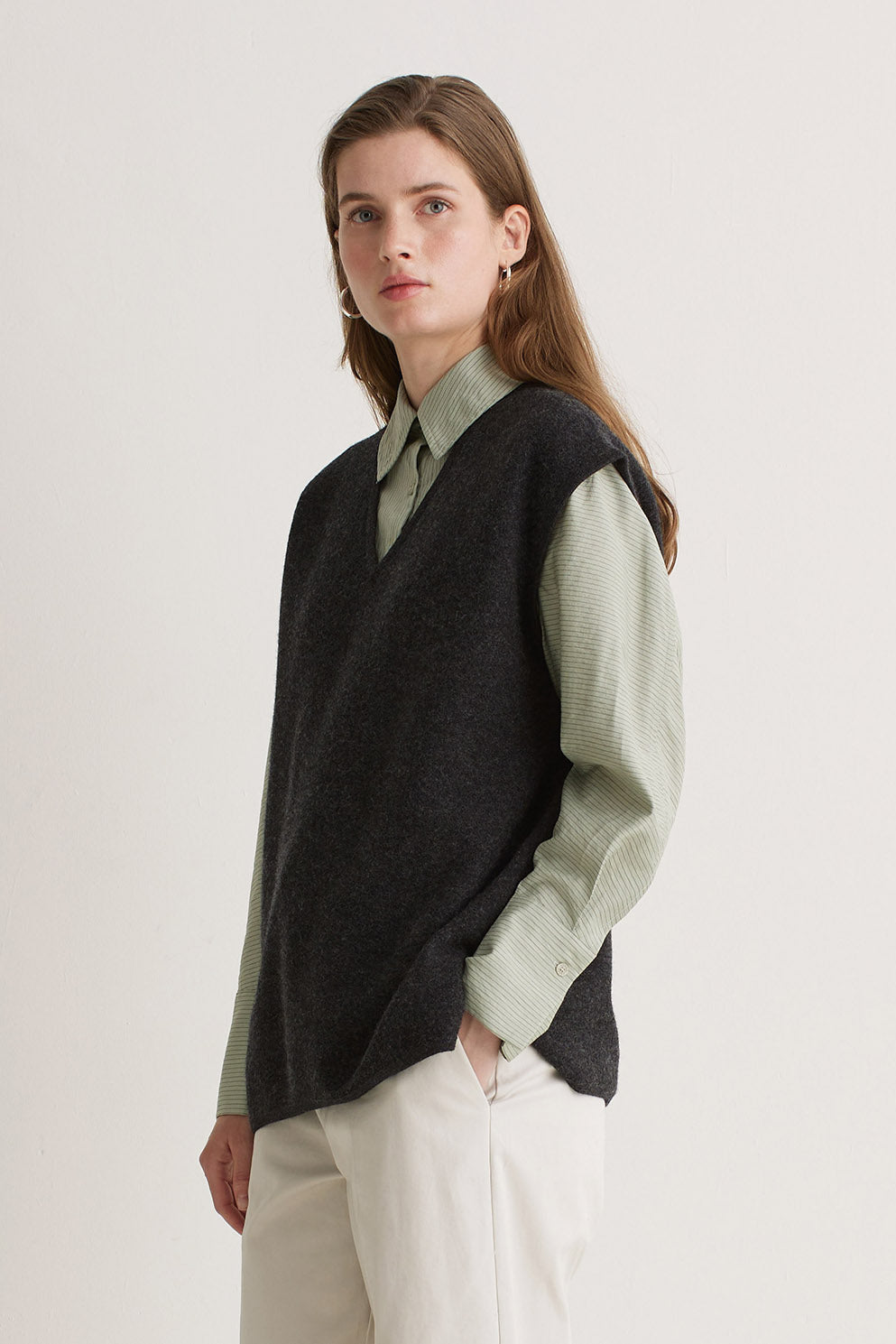 Woman wearing a black vest over a light green shirt with a white background