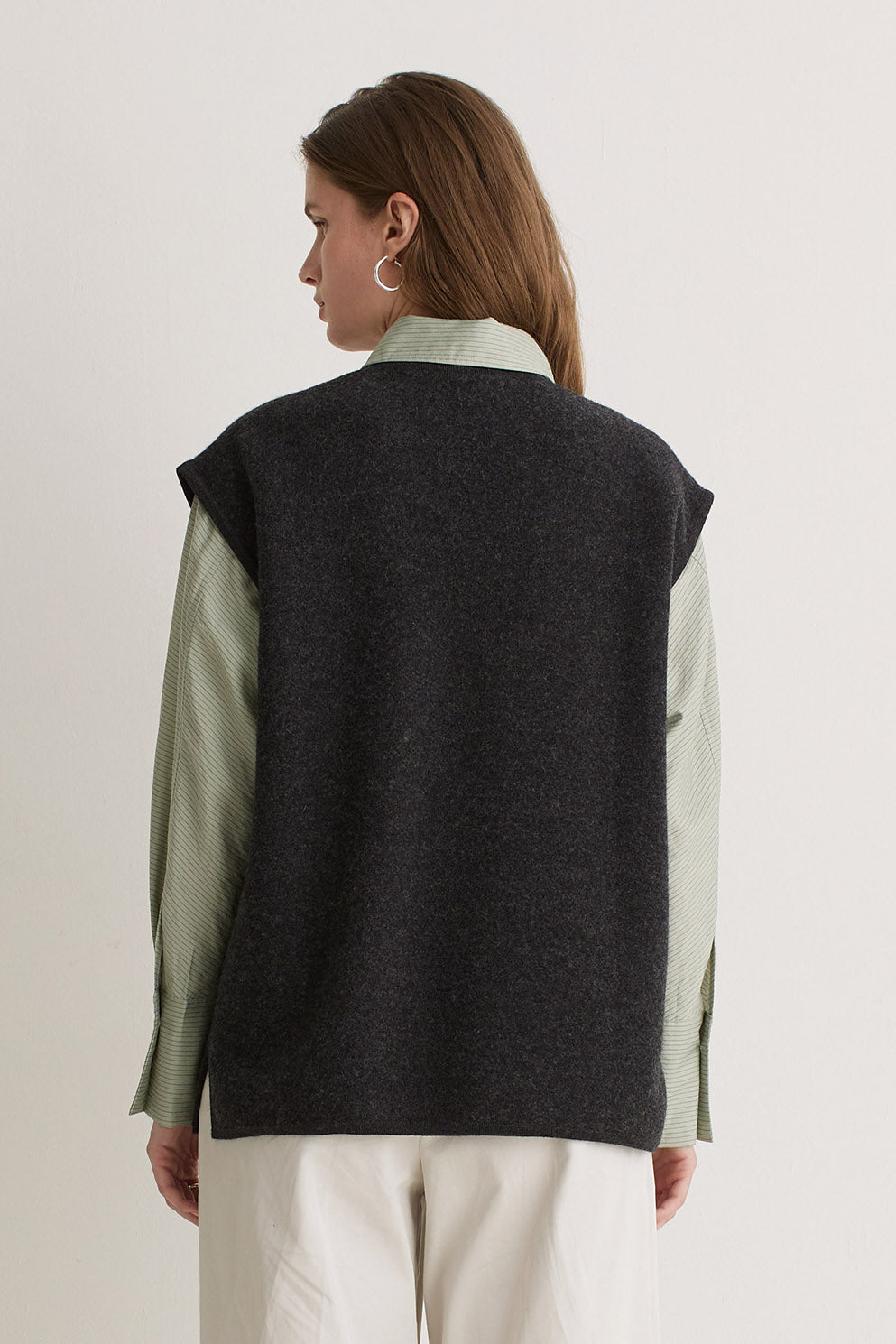 Person wearing a dark gray vest over a light green shirt on a plain background