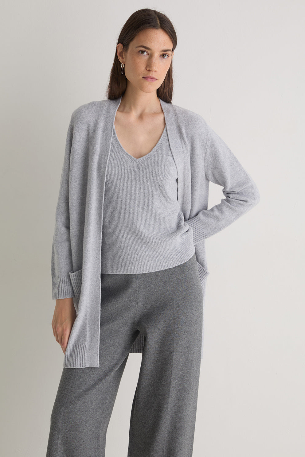 Woman wearing a gray cardigan over a matching top and pants on a plain background