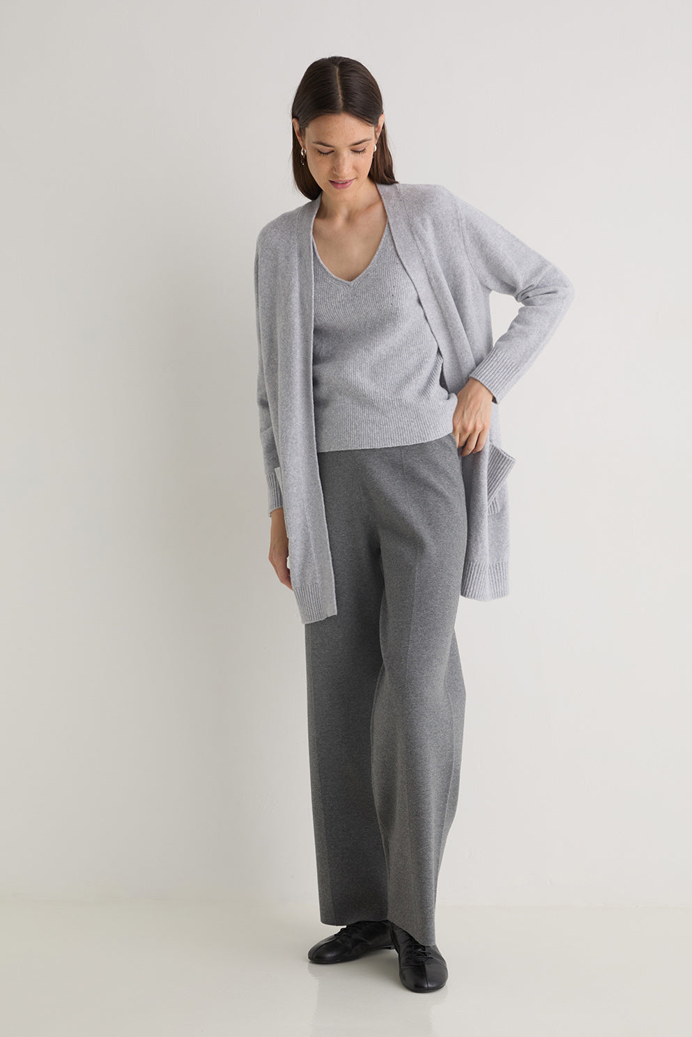 Woman wearing a gray cardigan, gray sweater, and gray pants on a white background