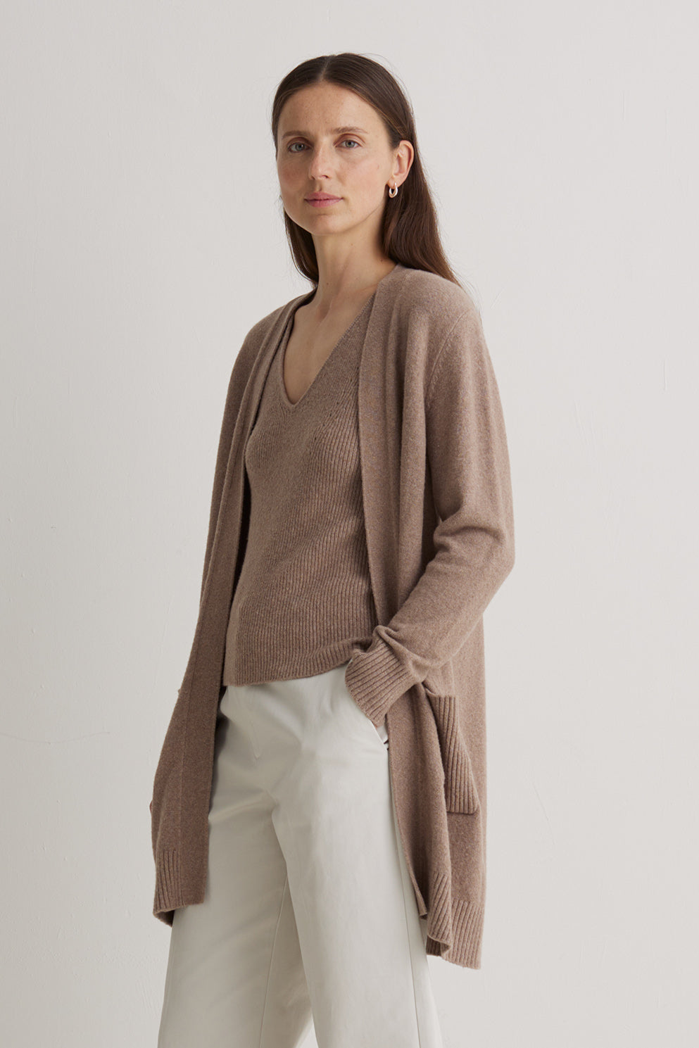 Woman wearing a brown cardigan and white pants on a plain background