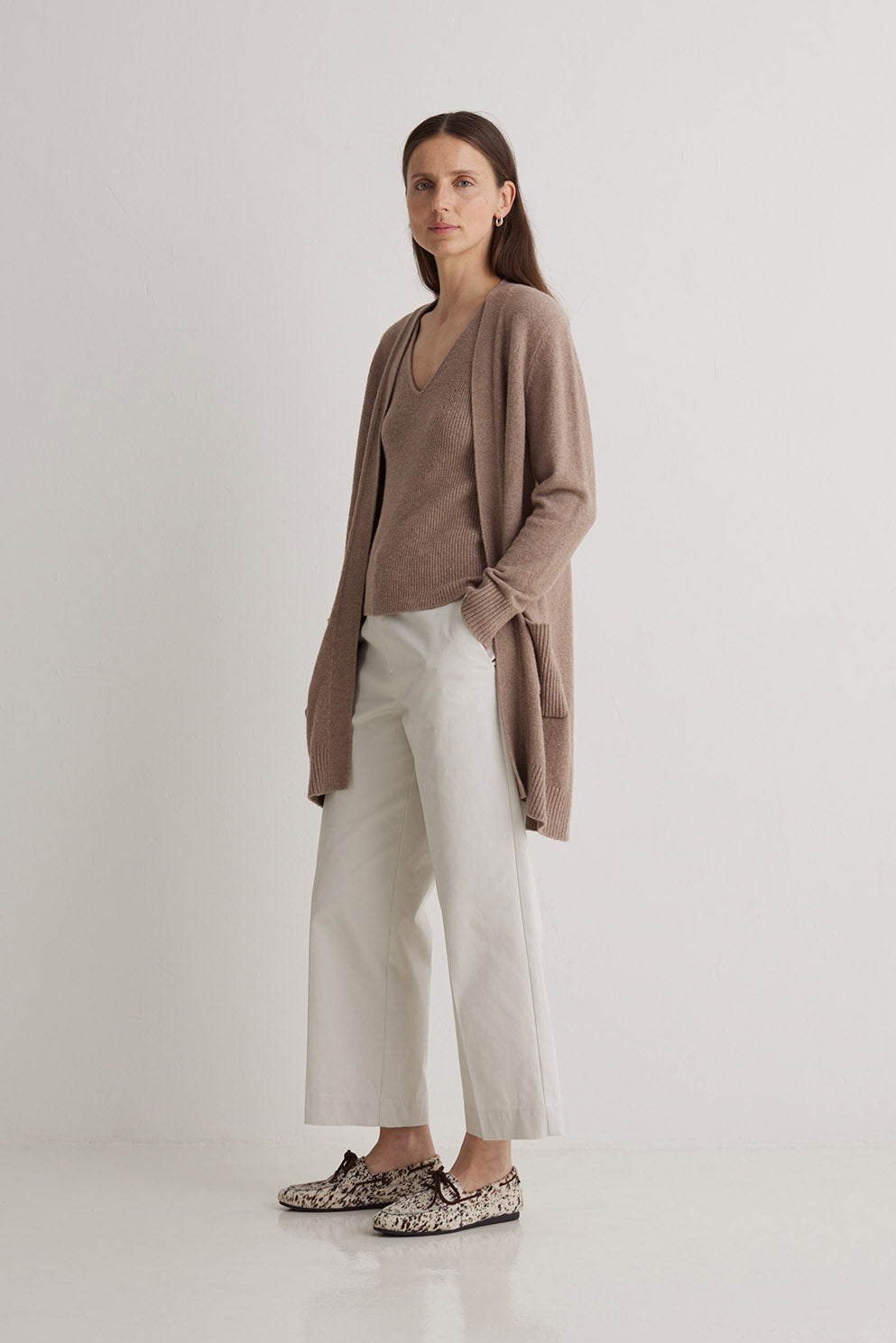 Woman wearing a brown cardigan, white pants, and patterned shoes on a white background