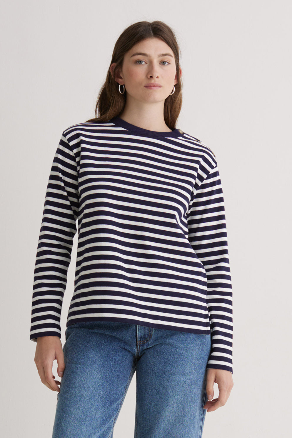Woman wearing a navy and white striped long sleeve tee with blue jeans on a plain background